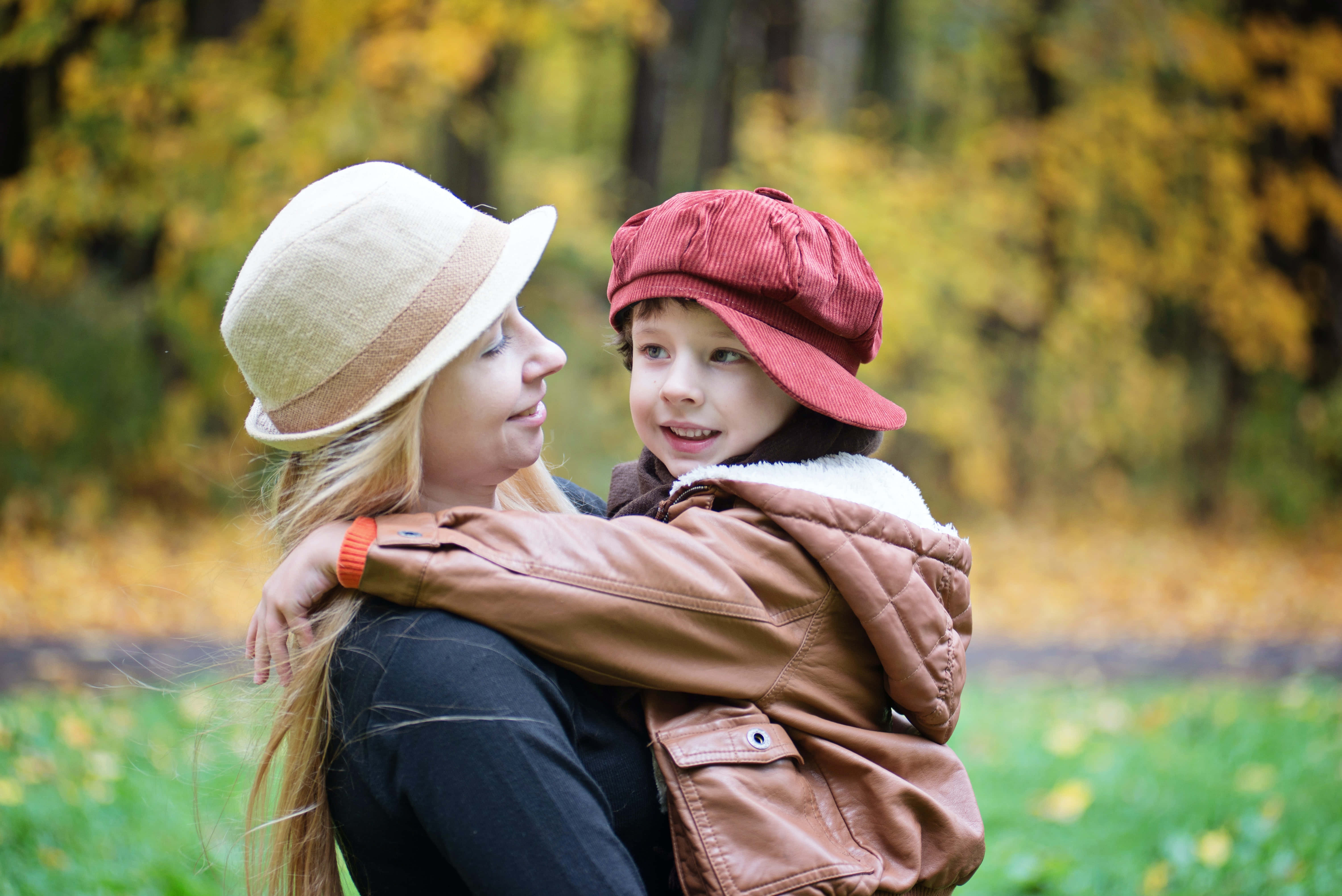 Mom 桌布 壁紙 — 一位女士和一個孩子在陽光明媚、金黃樹葉的秋日森林中溫暖地擁抱。