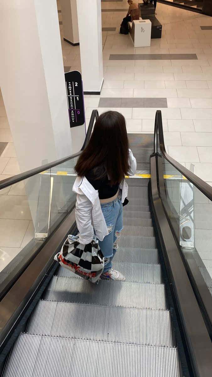 一位女士在商場內走下扶手電梯 壁紙