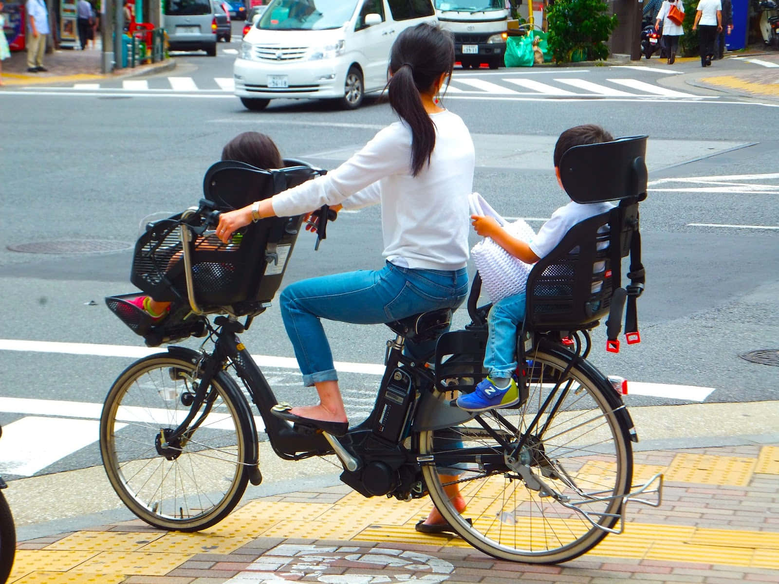 Bicycle 桌布 壁紙 — 一位女士在城市的街道上踩單車，後座和前座兒童座椅上各固定了一名兒童。