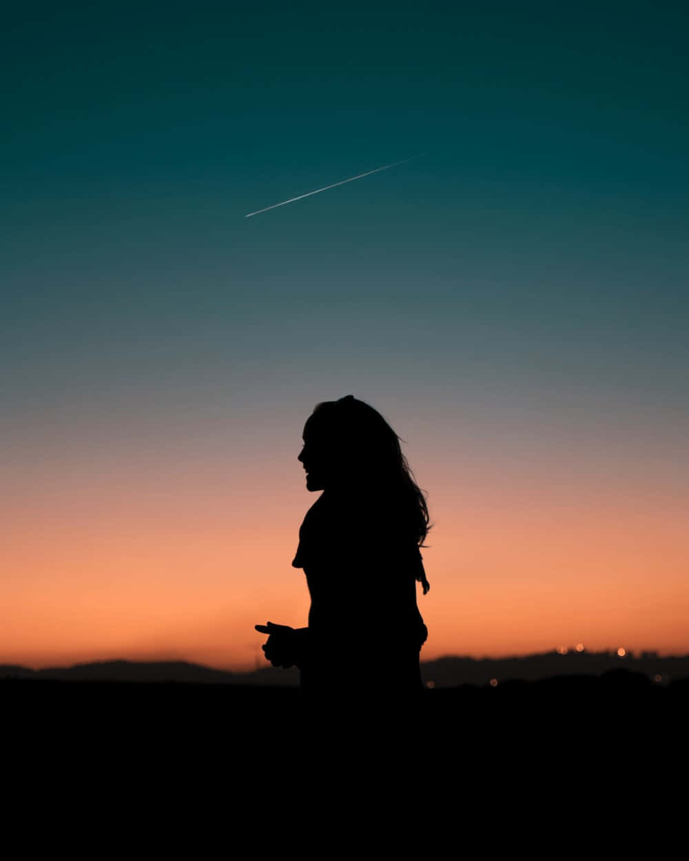 Sunset Silhouette 桌布 壁紙 — 一位女士在日落時站立的剪影，一條凝結尾跡劃過漸變的天空。