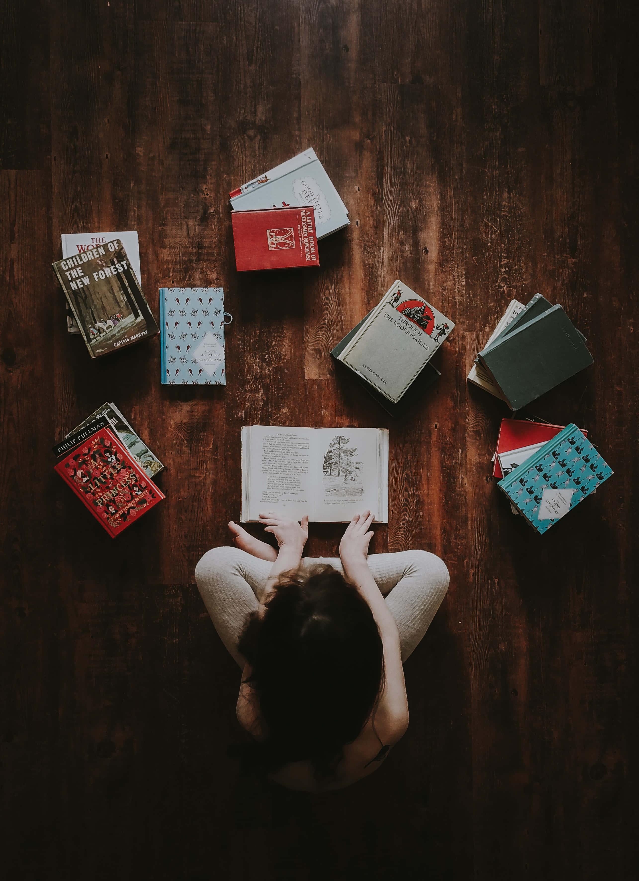 一位女士在木地板上閱讀一本書 壁紙