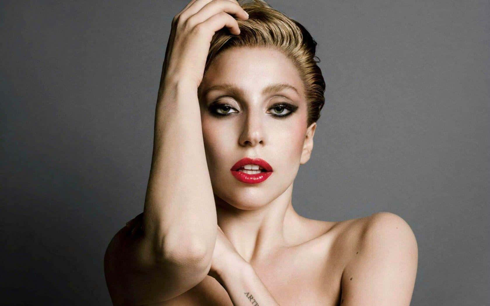 Lady Gaga 桌布 壁紙 — 一位女士在灰色背景前擺姿勢，擁有鮮豔的紅唇和煙燻眼妝，引人注目的肖像。