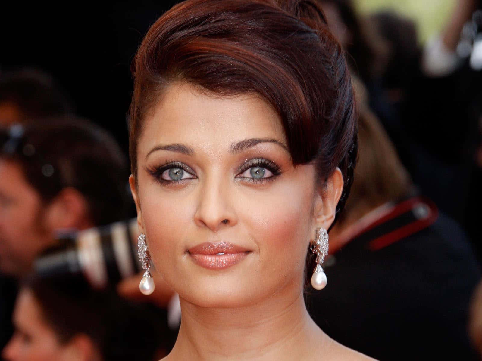 Aishwarya Rai 桌布 壁紙 — 一位女士在華麗活動中的特寫肖像，擁有引人注目的藍色眼睛和優雅的珍珠耳環。