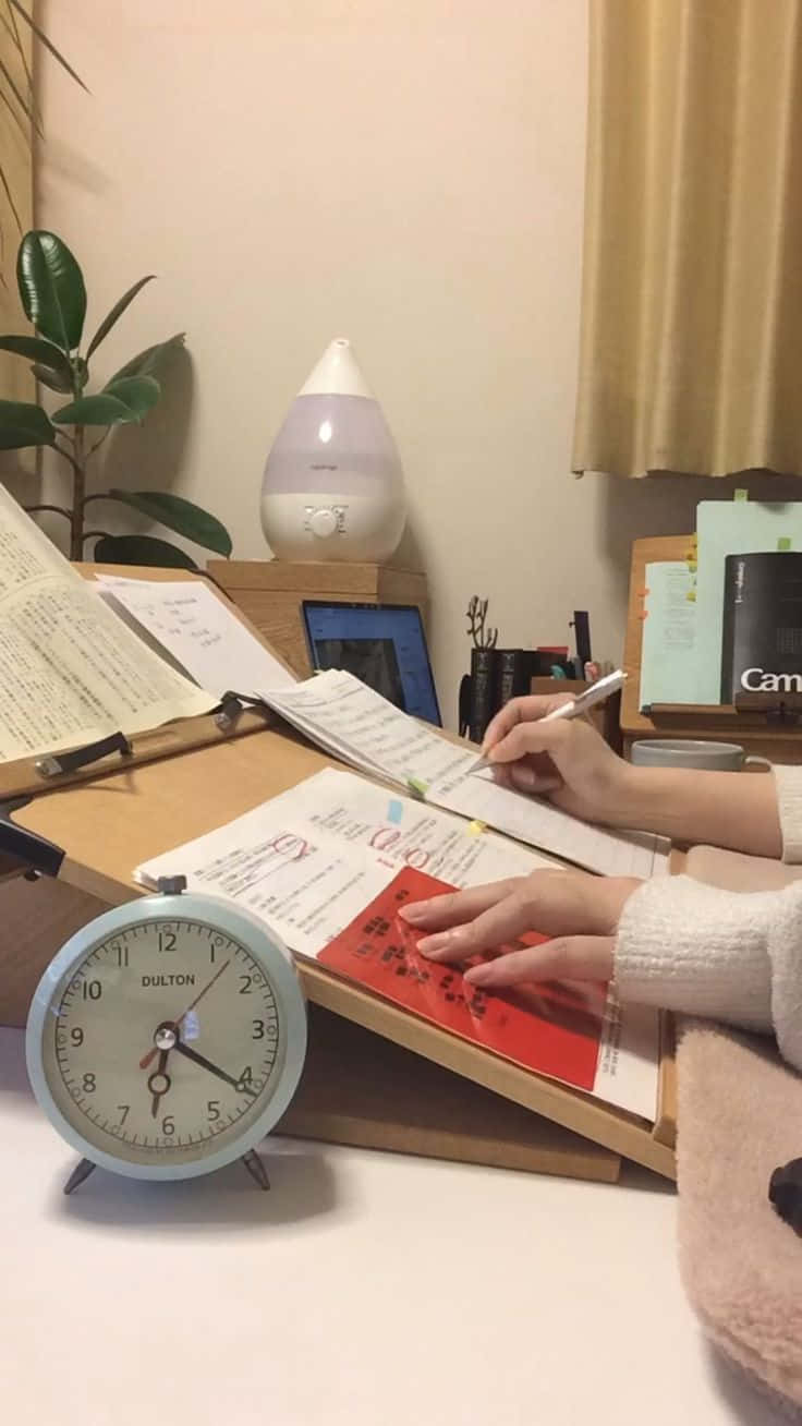一位女士坐在書桌前，旁邊有時鐘和文件 壁紙