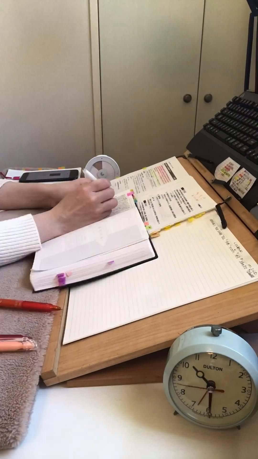 一位女士坐在書桌前，面前放著筆記本和時鐘 壁紙