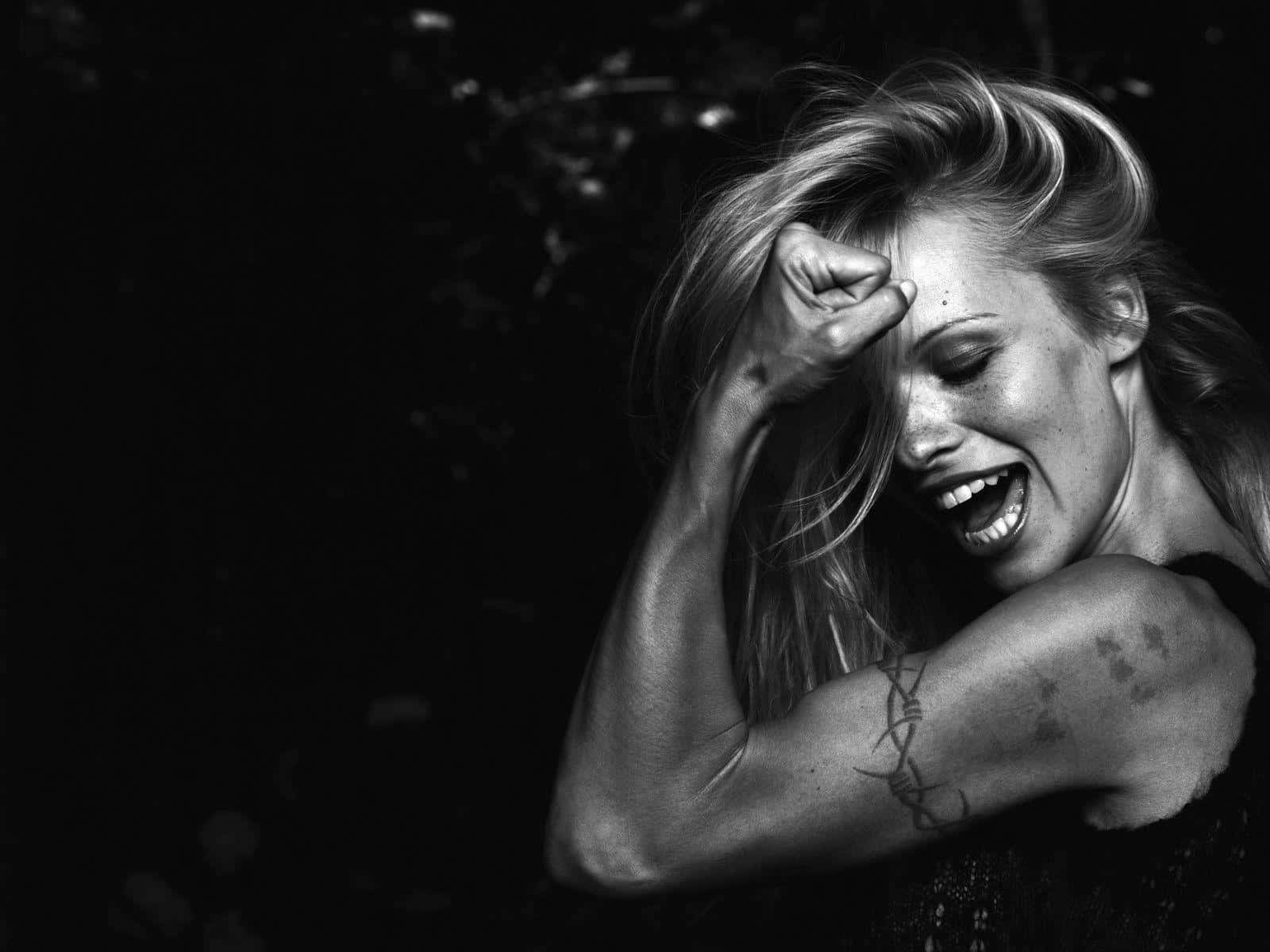 pamela anderson 桌布 壁紙 — 一位女士將手放在額頭上，在戲劇性的黑白肖像中開懷大笑。