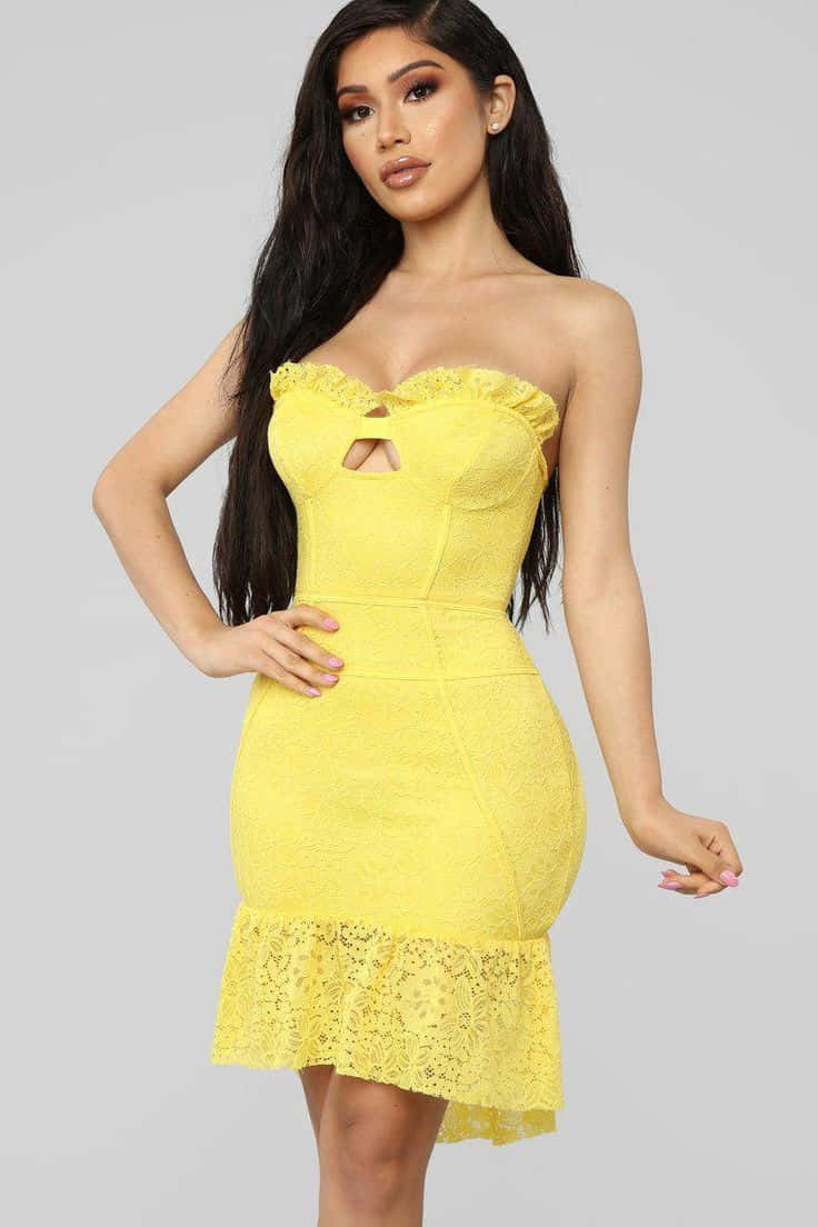 Yellow Fashion 桌布 壁紙 — 一位女士穿著鮮黃色蕾絲無肩帶連衣裙，荷葉邊下擺和鑰匙孔鏤空，在純灰色背景前自信地擺姿勢。