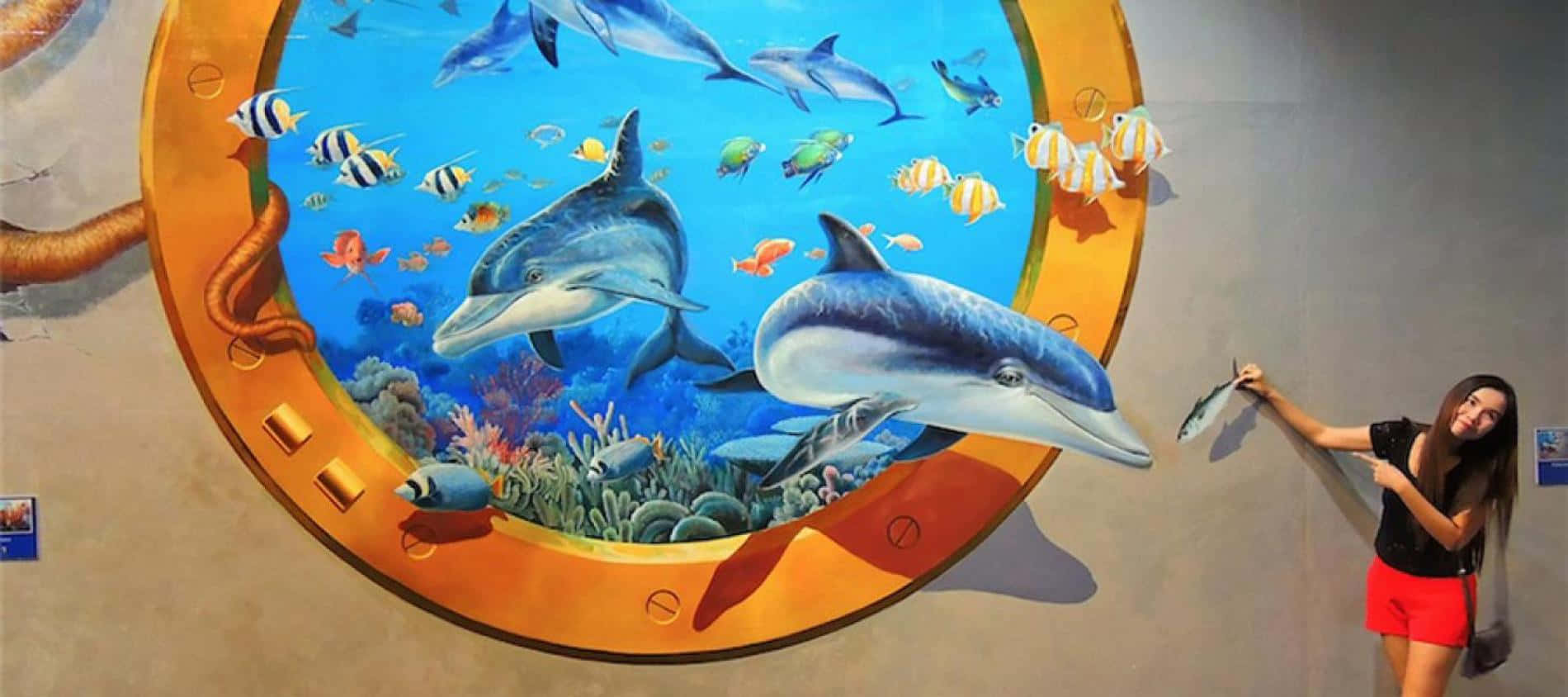 一位女士站在海豚與海洋生物壁畫旁 壁紙