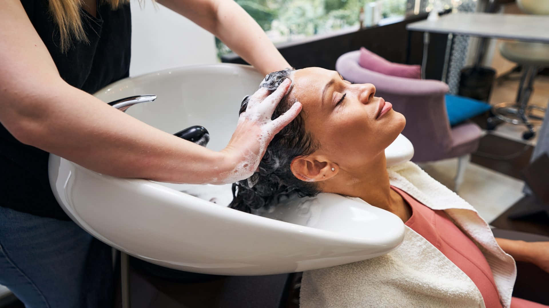 Hair Salon 桌布 壁紙 — 一位女士閉著眼睛放鬆，造型師在沙龍水槽中清洗她帶有肥皂泡的頭髮。