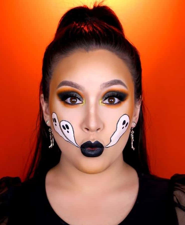 Halloween Makeup 桌布 壁紙 — 一位女性在充滿活力的橙色背景上，畫著大膽的萬聖節妝容，臉頰上有鬼魂圖案，嘴唇是黑色的。