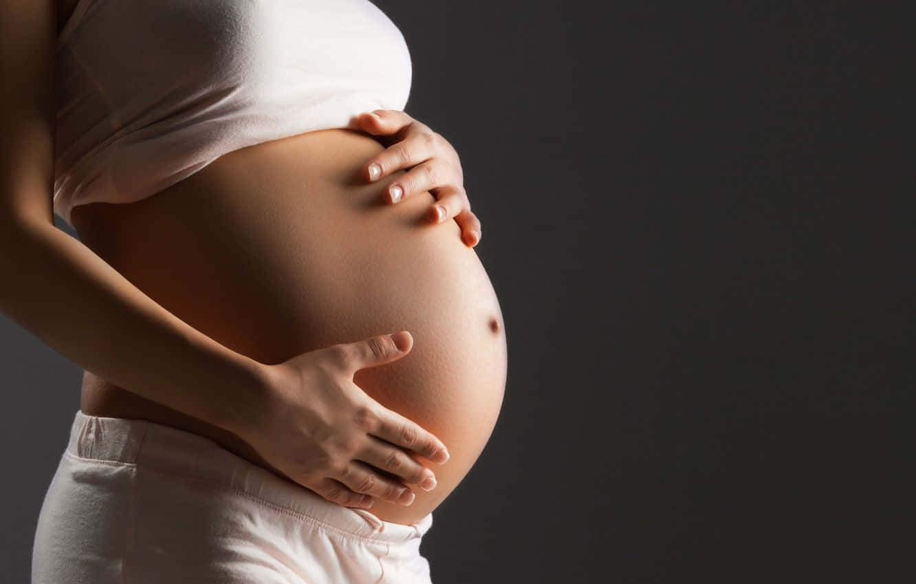pregnancy 桌布 壁紙 — 一位孕婦在深色攝影棚背景下用雙手輕輕捧著她圓潤的腹部。