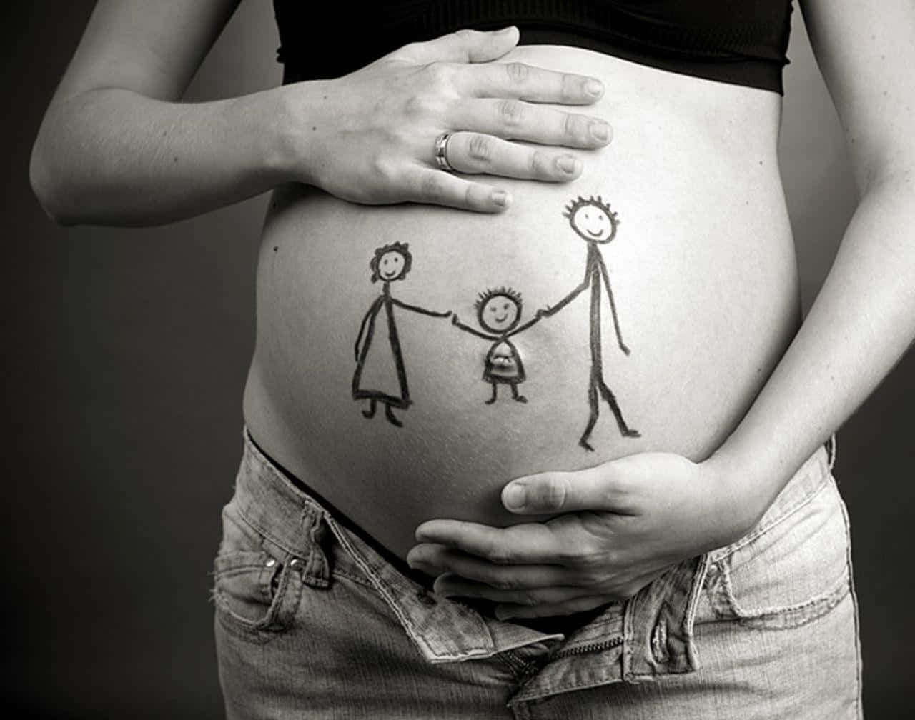 pregnancy 桌布 壁紙 — 一位孕婦的肚子上有一個簡單的線條畫，畫著手牽手的一家人，她的雙手輕輕捧著肚子，形成一幅黑白肖像。