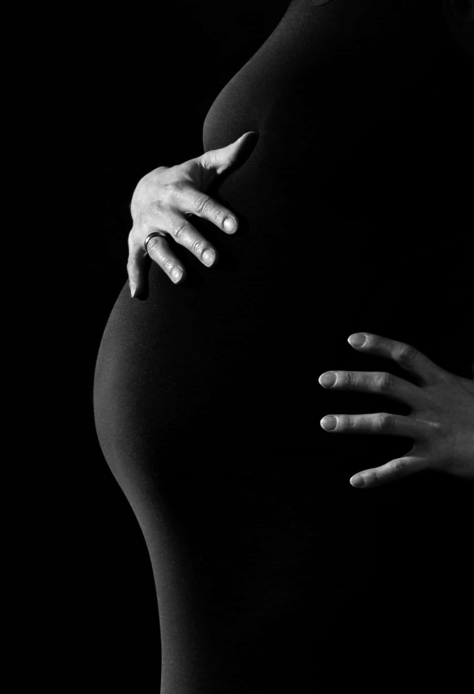 pregnancy 桌布 壁紙 — 一位孕婦的雙手在清晰的黑白工作室肖像中輕輕地捧著她圓潤的腹部。