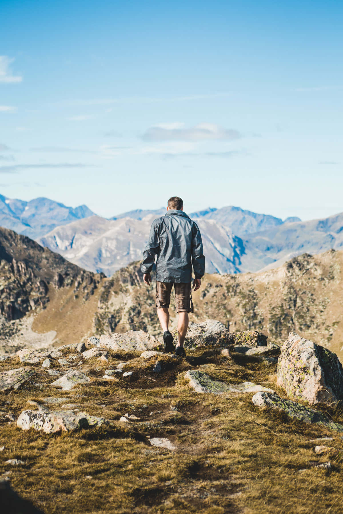 adventure 桌布 壁紙 — 一位孤獨的徒步者站在陽光明媚的山脊上，俯瞰著晴朗藍天下遙遠的山峰。