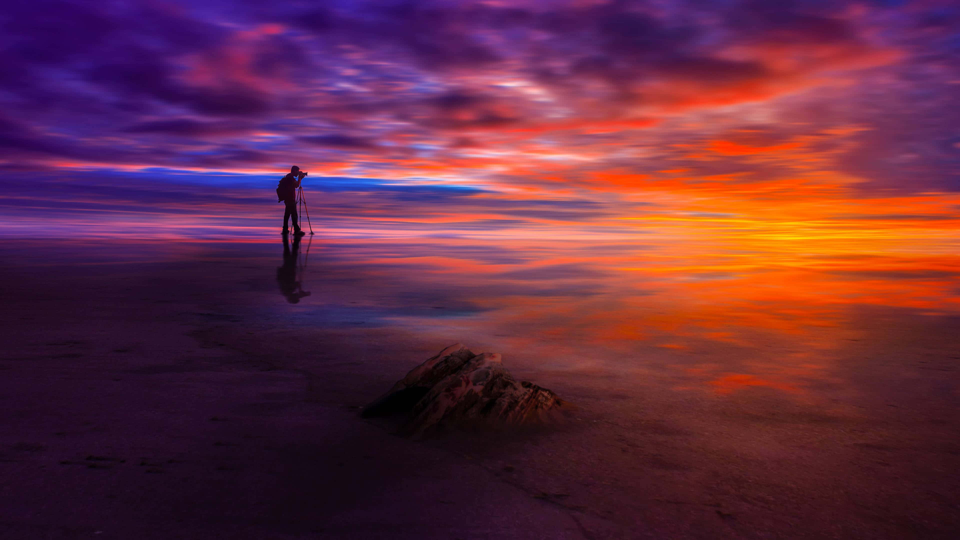 Sunset Photography 桌布 壁紙 — 一位孤獨的攝影師在日落時站在反射的鹽灘上，捕捉水中倒映的鮮豔紫色、橙色和藍色天空。