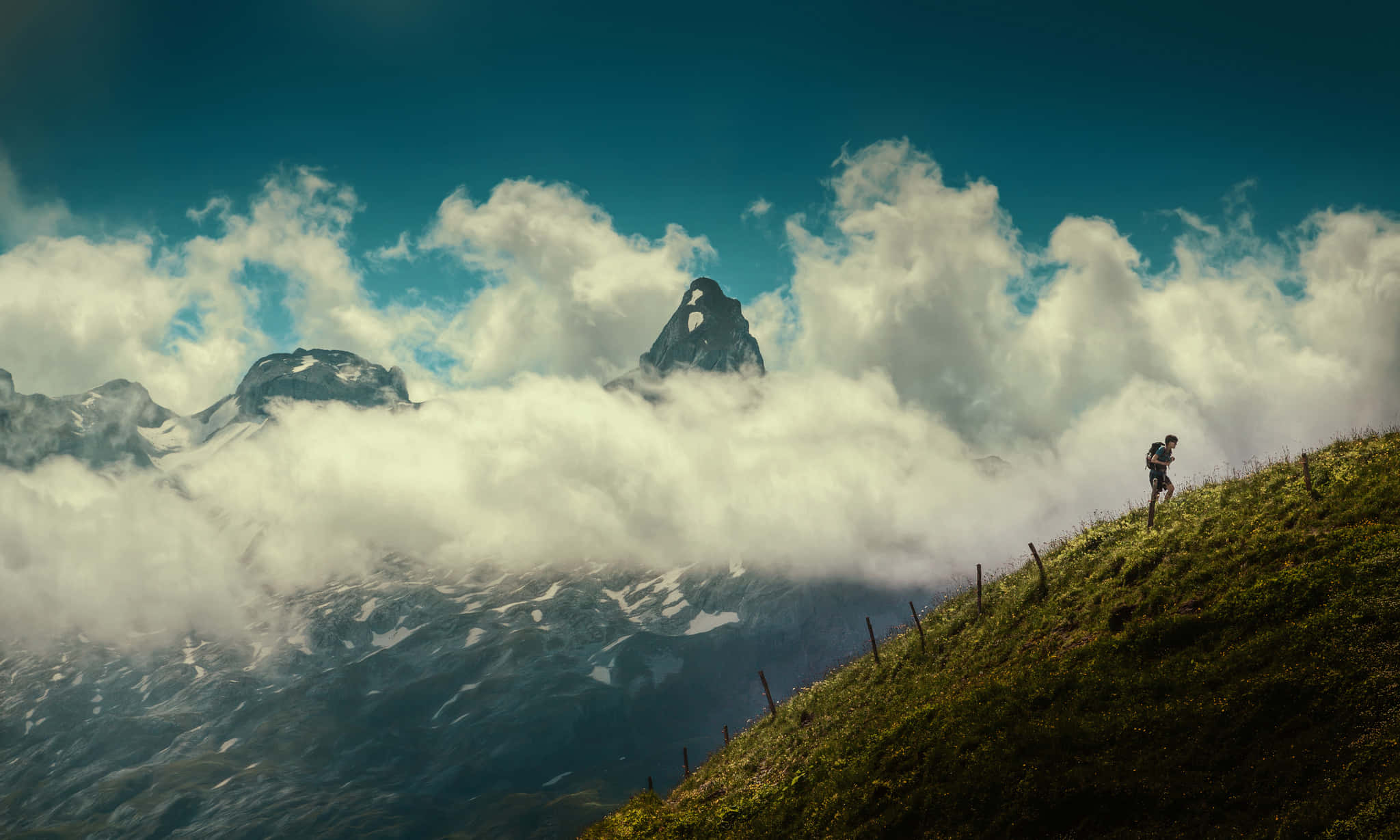 Hiking 桌布 壁紙 — 一位孤獨的遠足者攀爬著長滿草的山脊，雲霧在下方翻騰，積雪的山峰刺破天際。