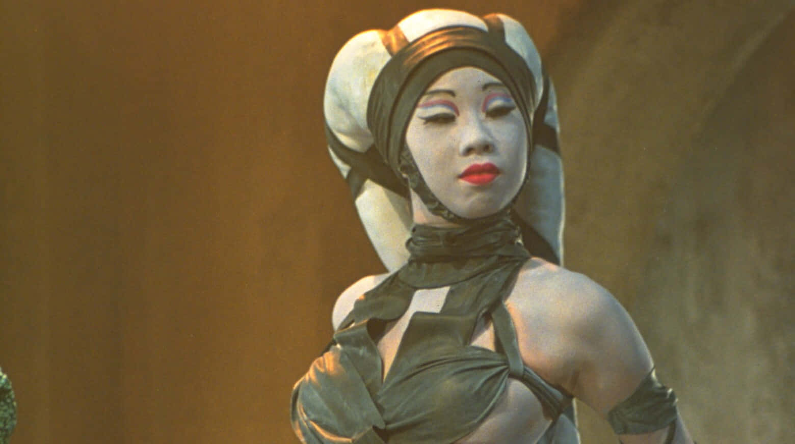 Twi'lek 桌布 壁紙 — 一位寧靜的外星女性，擁有白色皮膚和紅色嘴唇，戴著頭巾和深色服裝，背景是溫暖的棕色。