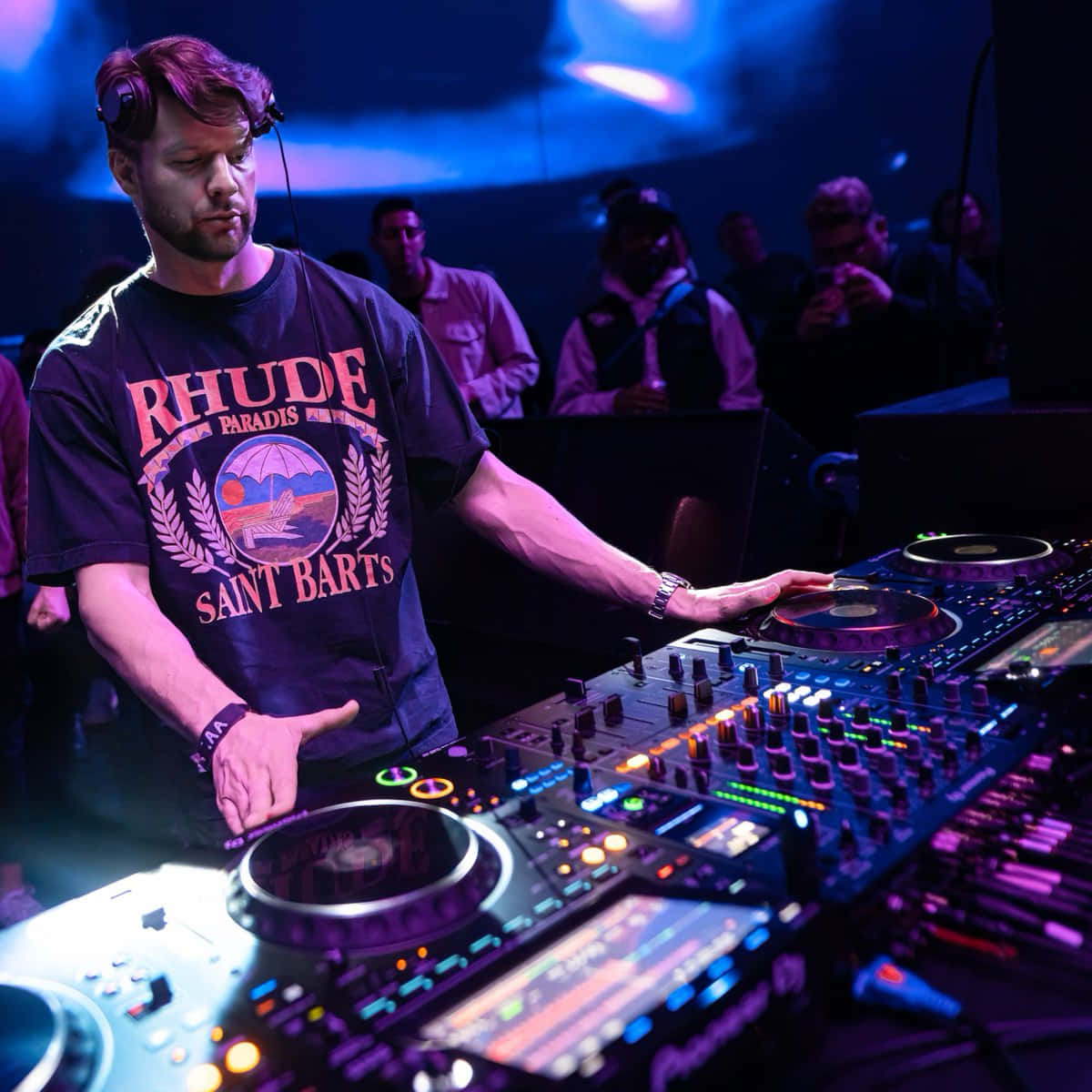 DJ 桌布 壁紙 — 一位專注的DJ在昏暗的俱樂部中，沐浴在藍色和紫色的燈光下，操控著發光的唱盤和混音器。