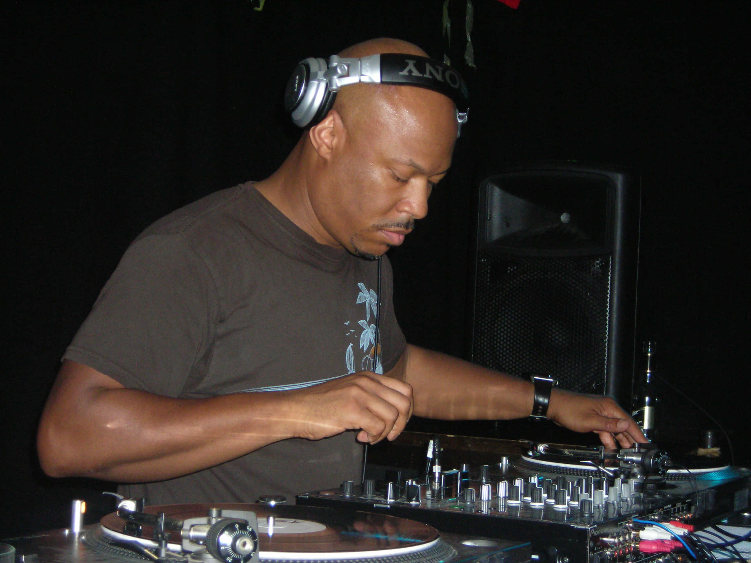 DJ 桌布 壁紙 — 一位專注的DJ戴著sony耳機，在昏暗的俱樂部燈光下於唱盤和混音器上混音。