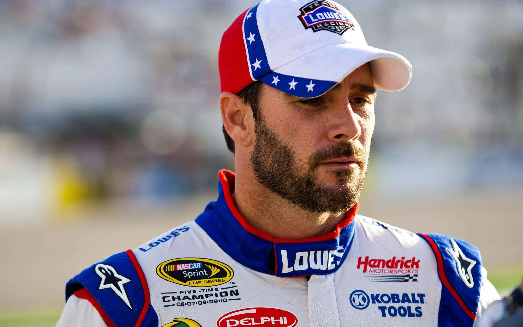 Jimmie Johnson 桌布 壁紙 — 一位專注的NASCAR車手，身穿藍白紅賽車服，帶有贊助商標誌，專注地凝視前方的賽道。