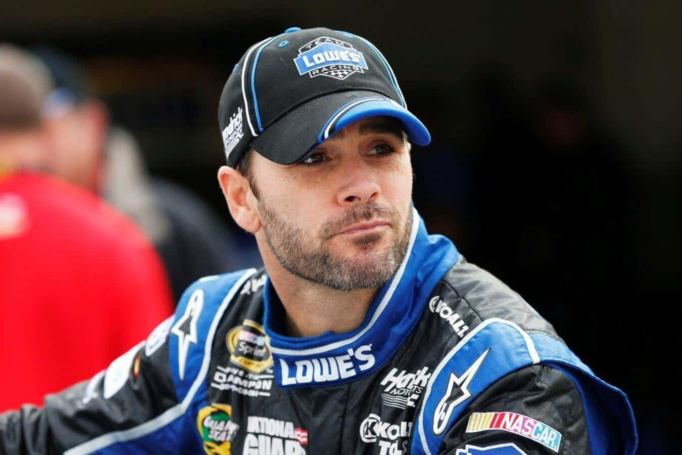 Jimmie Johnson 桌布 壁紙 — 一位專注的NASCAR車手，身穿Lowe's賽車服和帽子，在賽事中凝視前方。