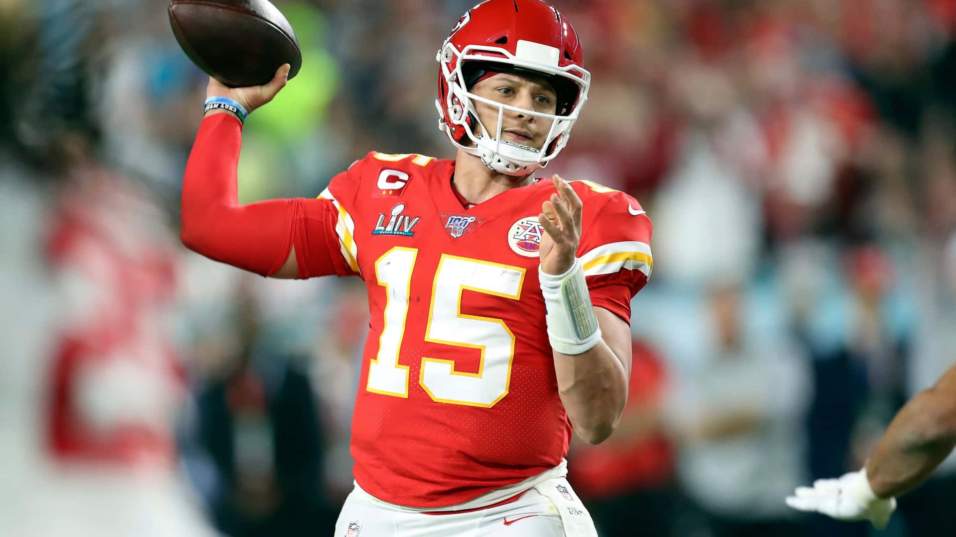 身穿紅色球衣的NFL四分衛在夜間比賽中擲出美式足球。 — 帕特里克·馬霍姆斯 壁紙