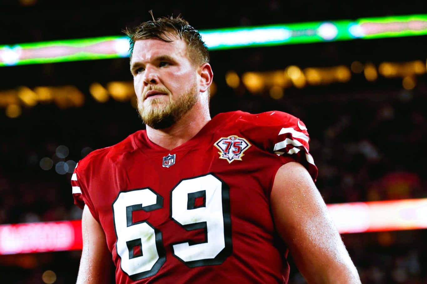 Mike Mcglinchey 桌布 壁紙 — 一位專注的NFL進攻截鋒身穿紅色69號球衣，在夜間比賽中站在球場燈光下。