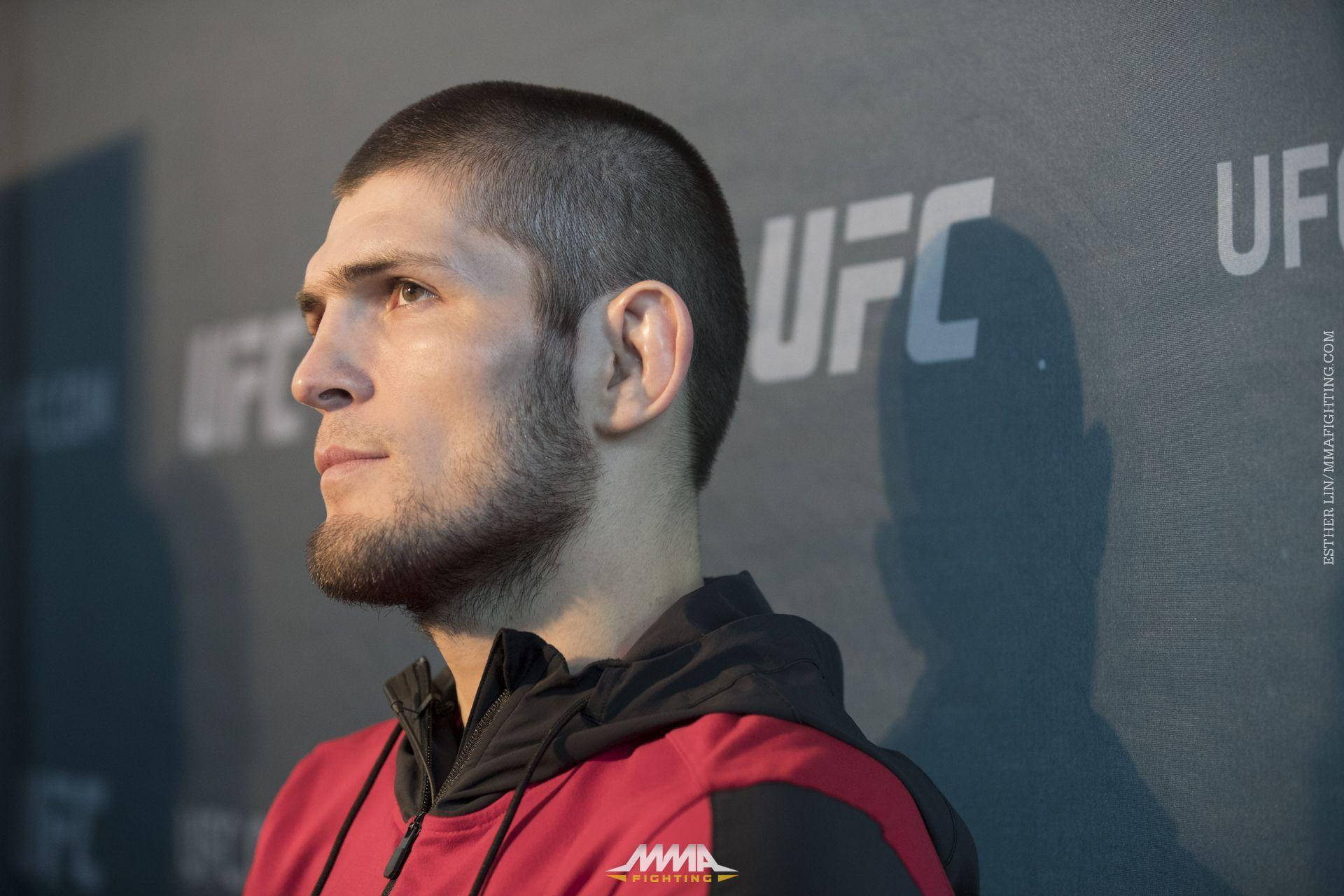UFC 桌布 壁紙 — 一位專注的UFC拳手穿著紅黑連帽衫，凝視著記者會背景。