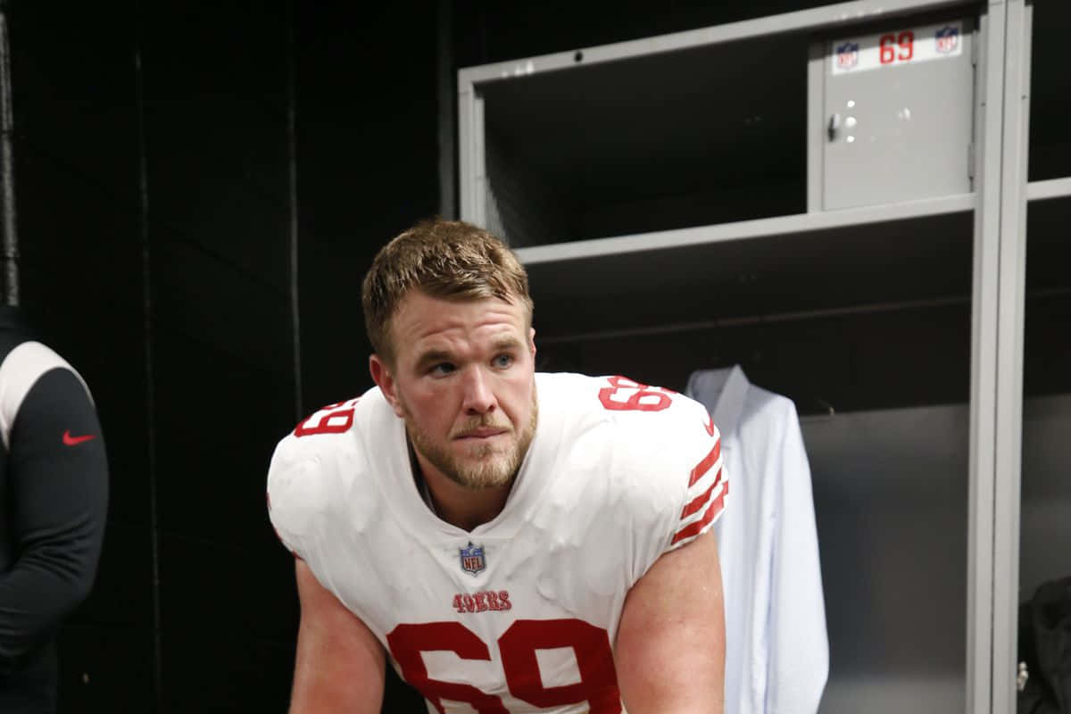 Mike Mcglinchey 桌布 壁紙 — 一位專注的三藩市49人美式足球員，身穿白色69號球衣，在昏暗的更衣室裡向前傾。