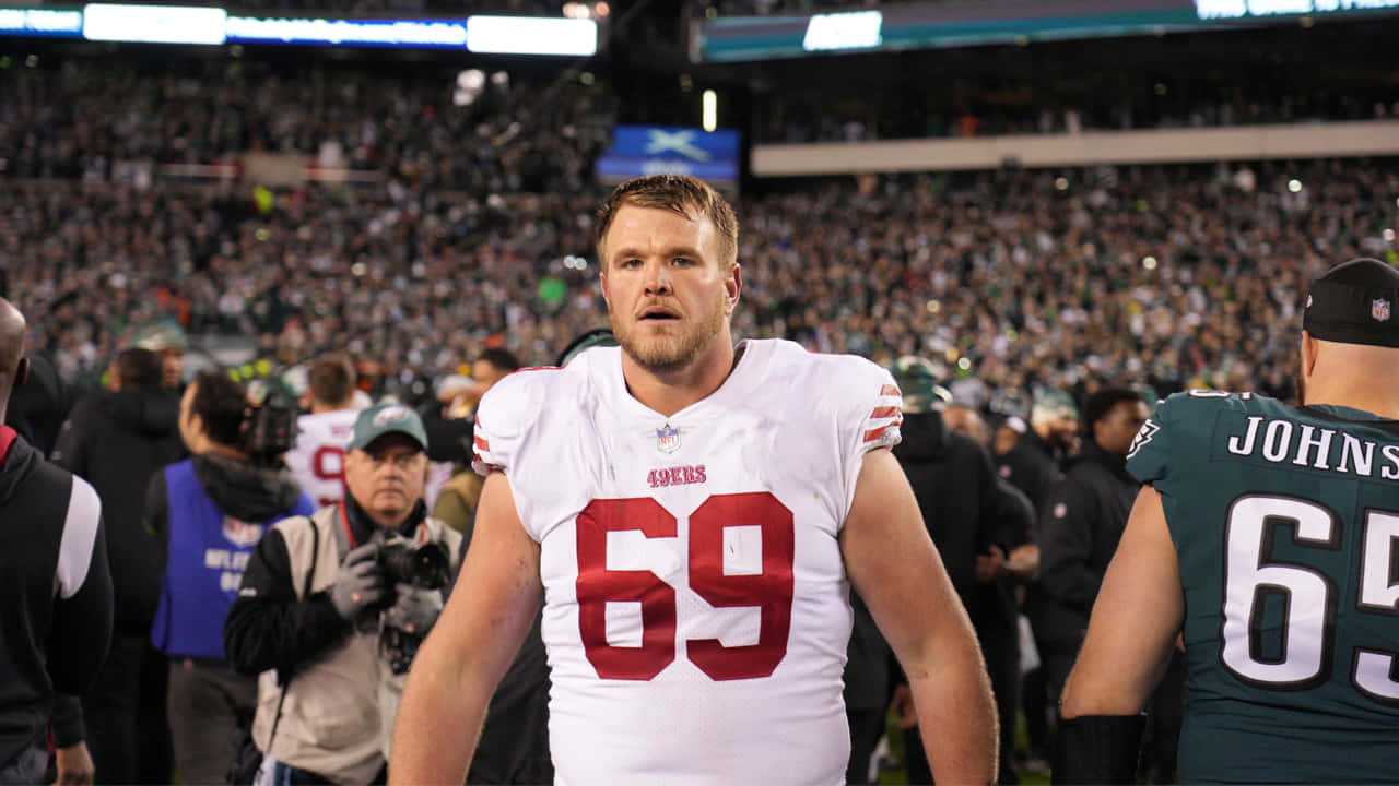 Mike Mcglinchey 桌布 壁紙 — 一位專注的三藩市四九人美式足球員身穿白色69號球衣，在比賽期間站在球場上，身後是座無虛席的體育場。