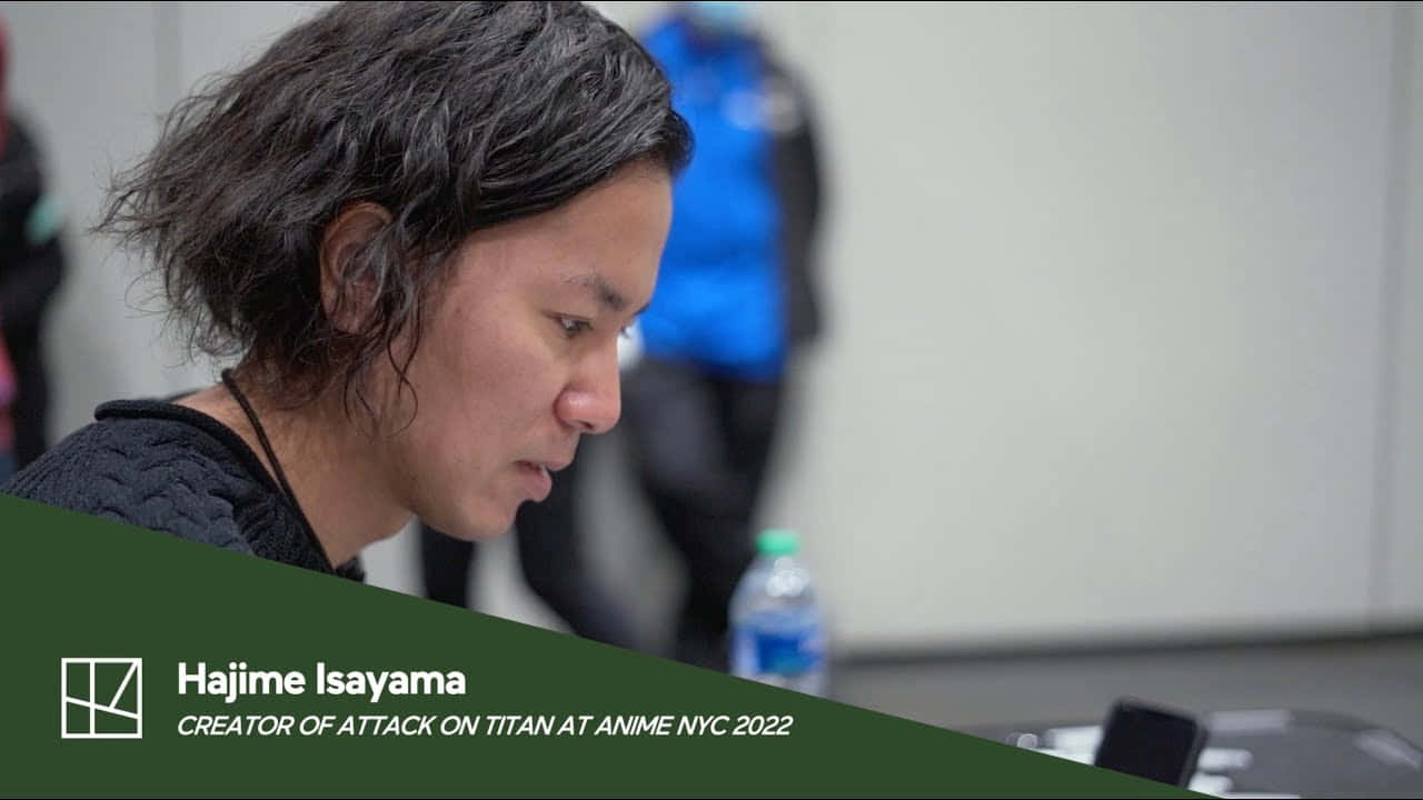 Isayama Hajime 桌布 壁紙 — 一位專注的動漫創作者，深色頭髮，在會議座談會上身體前傾，旁邊有一個水瓶。