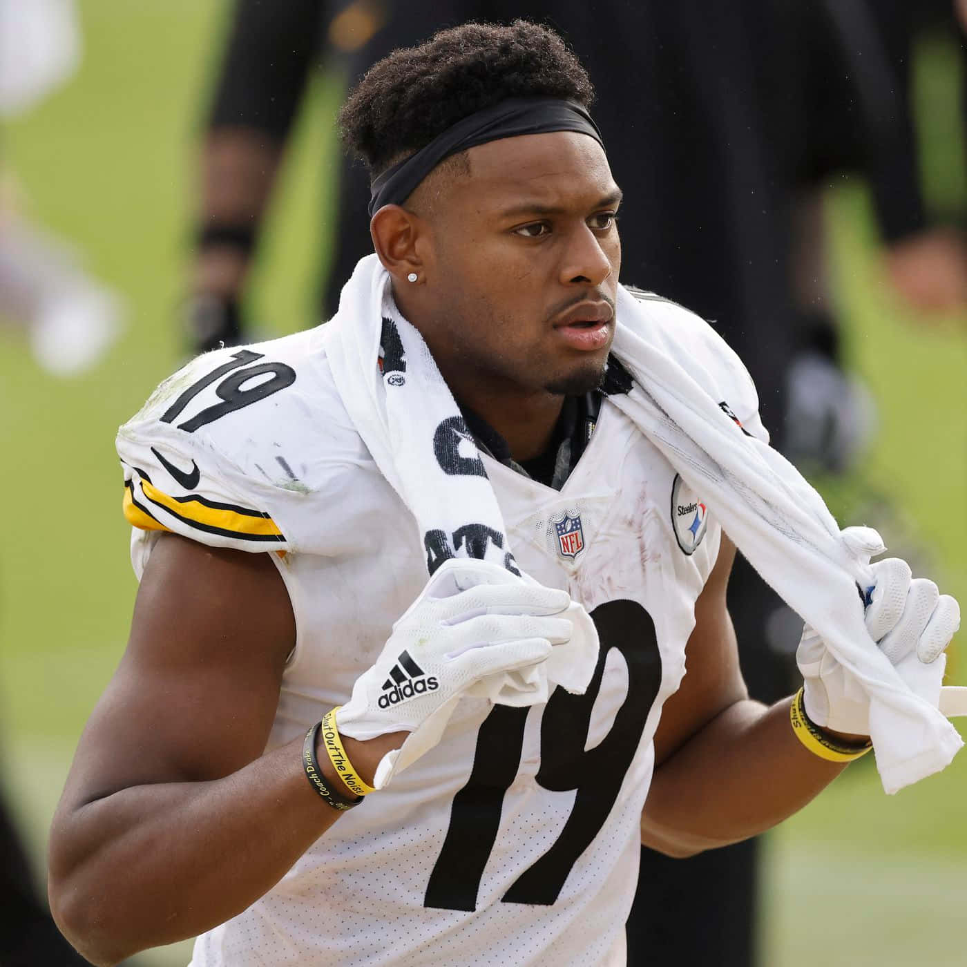 Juju Smith Schuster 桌布 壁紙 — 一位專注的匹茲堡鋼人隊美式足球員，身穿19號球衣，在明亮的球場上用毛巾擦汗。