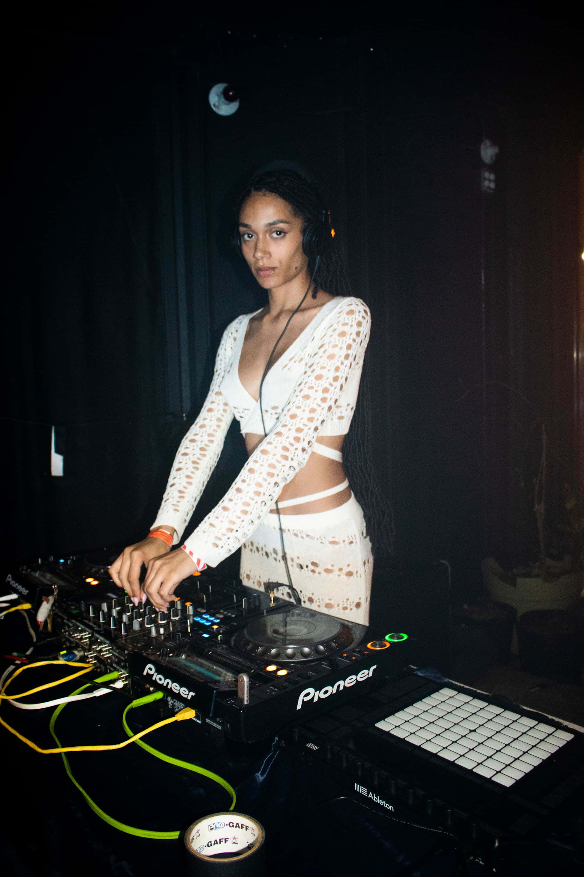 DJ 桌布 壁紙 — 一位專注的女DJ穿著白色蕾絲服裝，在昏暗的俱樂部燈光下操作Pioneer DJ設備。