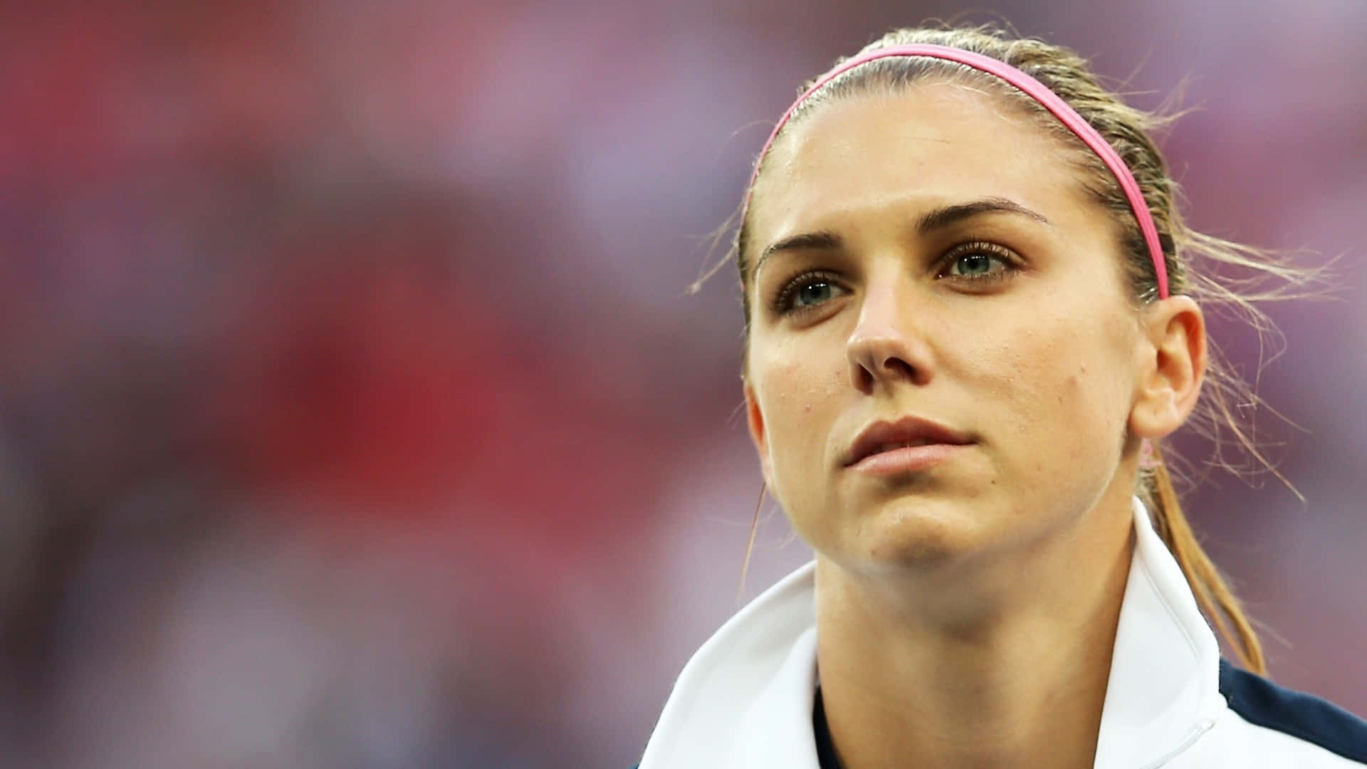 Alex Morgan 桌布 壁紙 — 一位專注的女運動員戴著粉紅色頭帶，在日間體育賽事中凝視著。