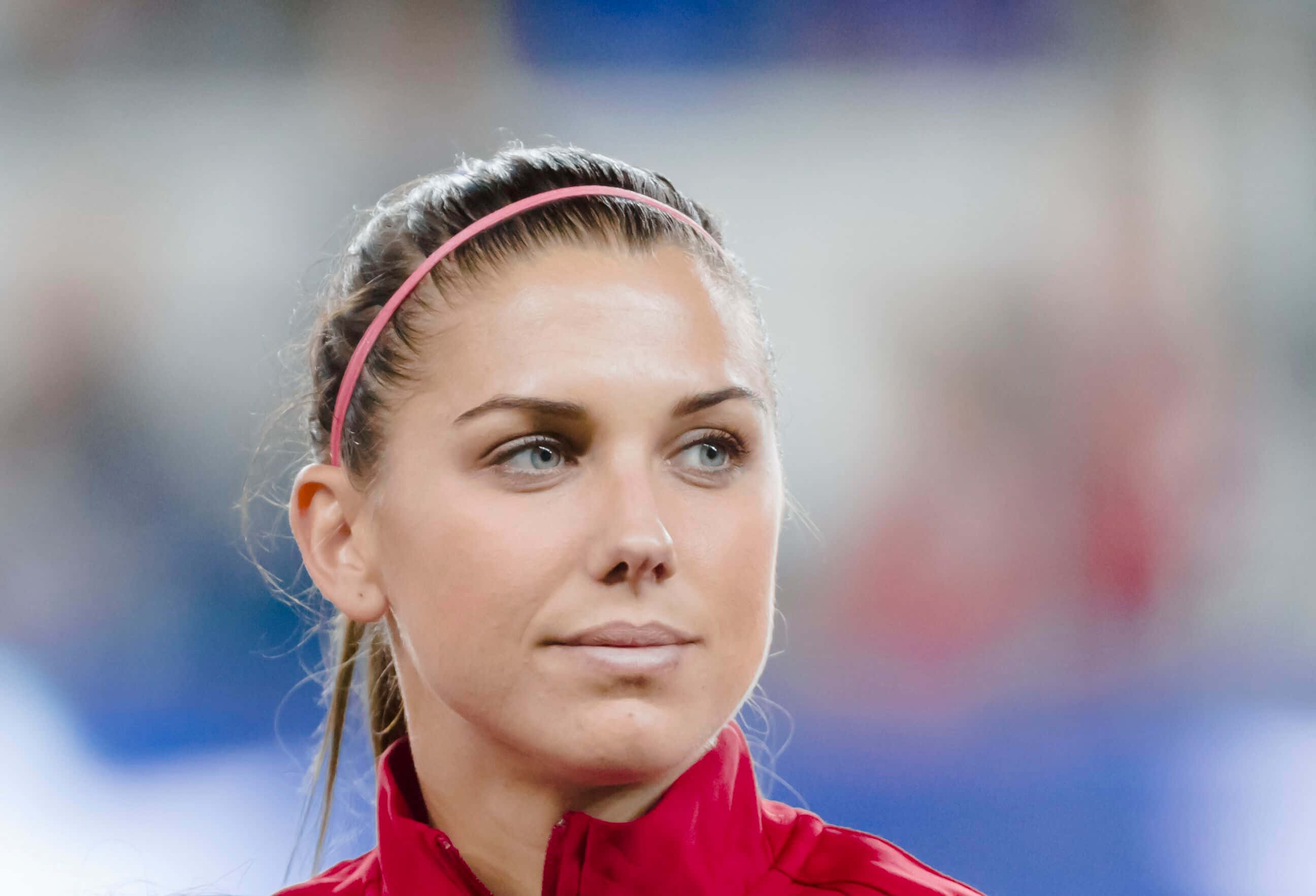 Alex Morgan 桌布 壁紙 — 一位專注的女運動員穿著紅色外套和粉紅色頭帶，在體育賽事中凝視著。