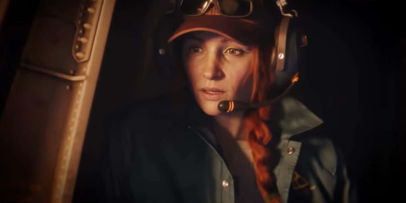 Rainbow Six Siege Ash 桌布 壁紙 — 一位專注的女飛行員，紅色辮子，戴著耳機和帽子，在昏暗的駕駛艙內，被溫暖的環境光線照亮。