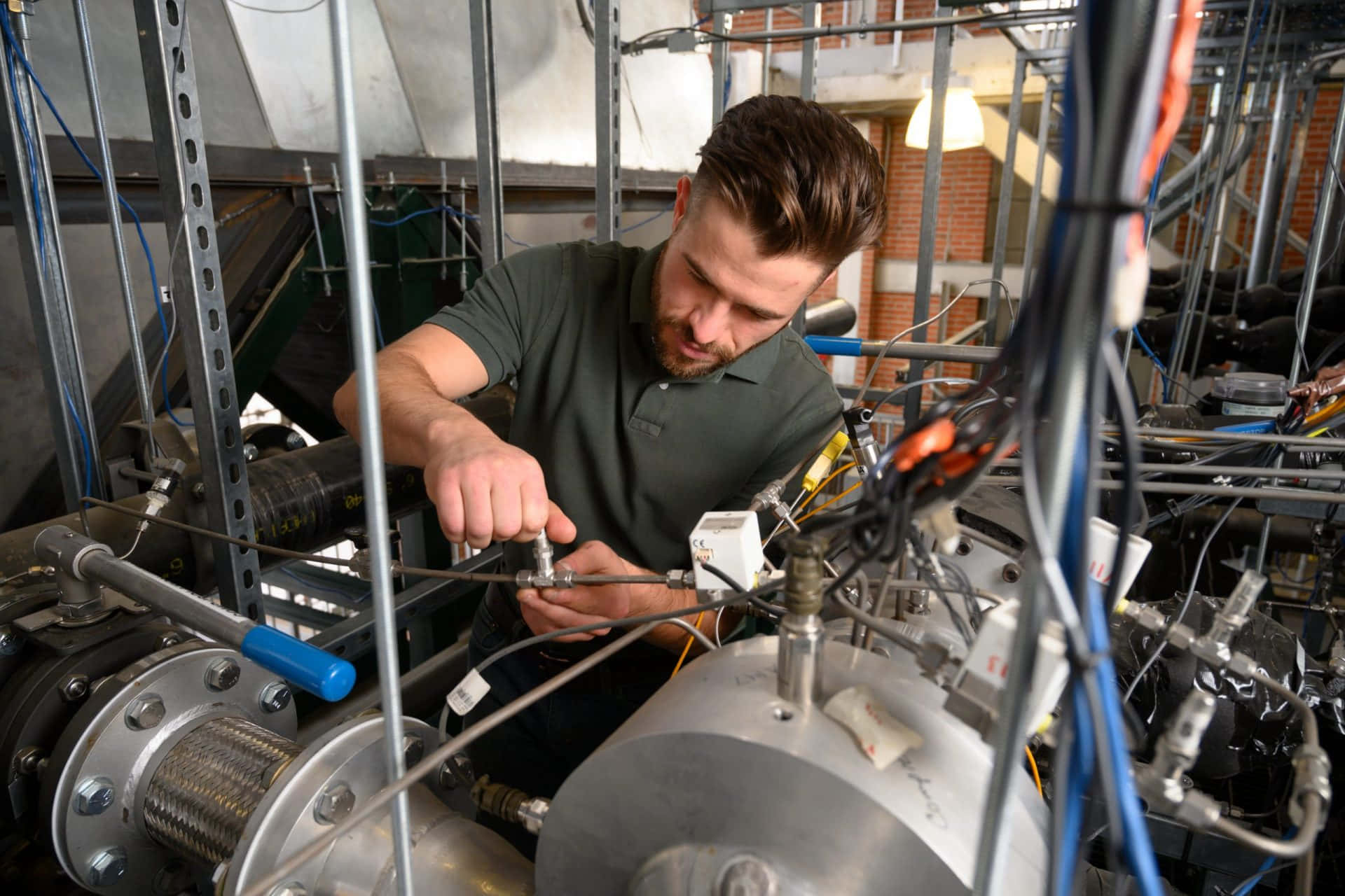 Engineer 桌布 壁紙 — 一位專注的技術人員在雜亂的實驗室環境中調整複雜工業機械上的閥門。