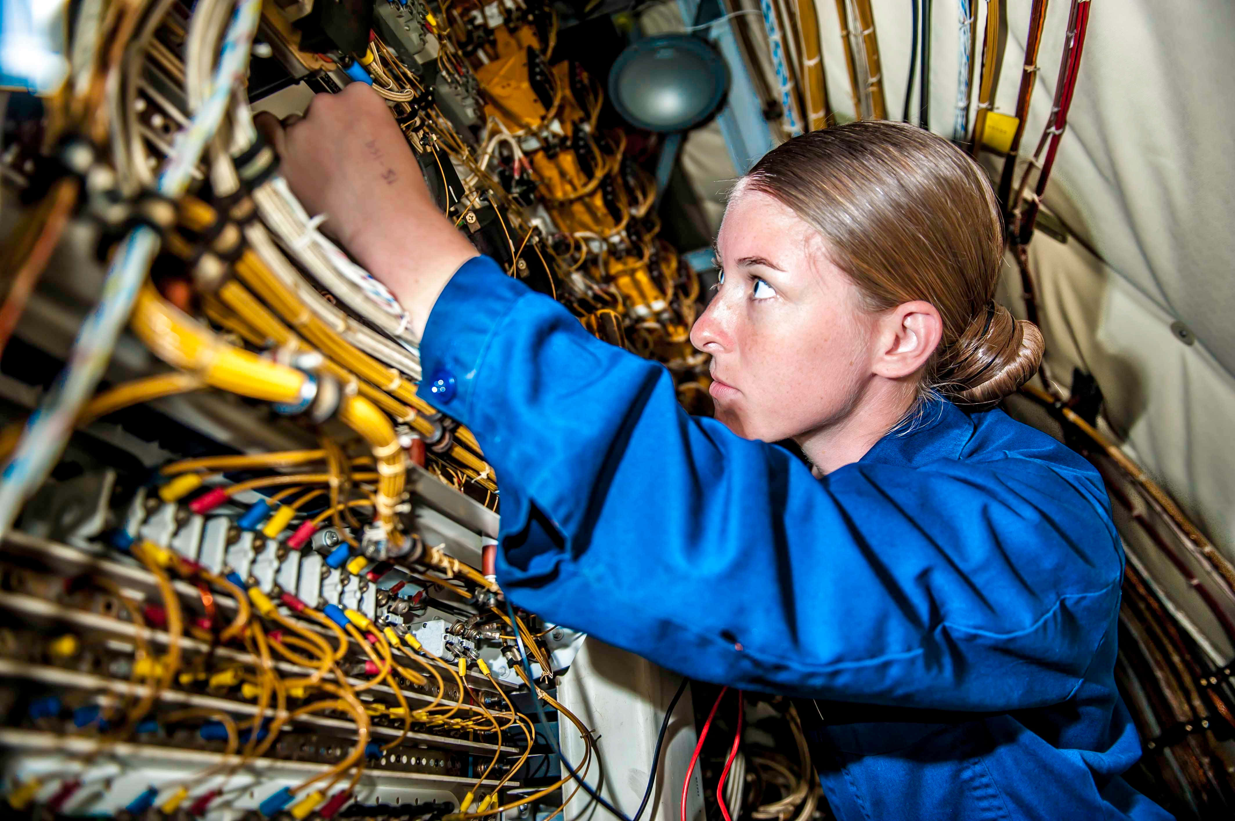 Engineer 桌布 壁紙 — 一位專注的技術人員身穿藍色連身工作服，在技術外殼內細心地處理密集纏繞的彩色電線和電纜。