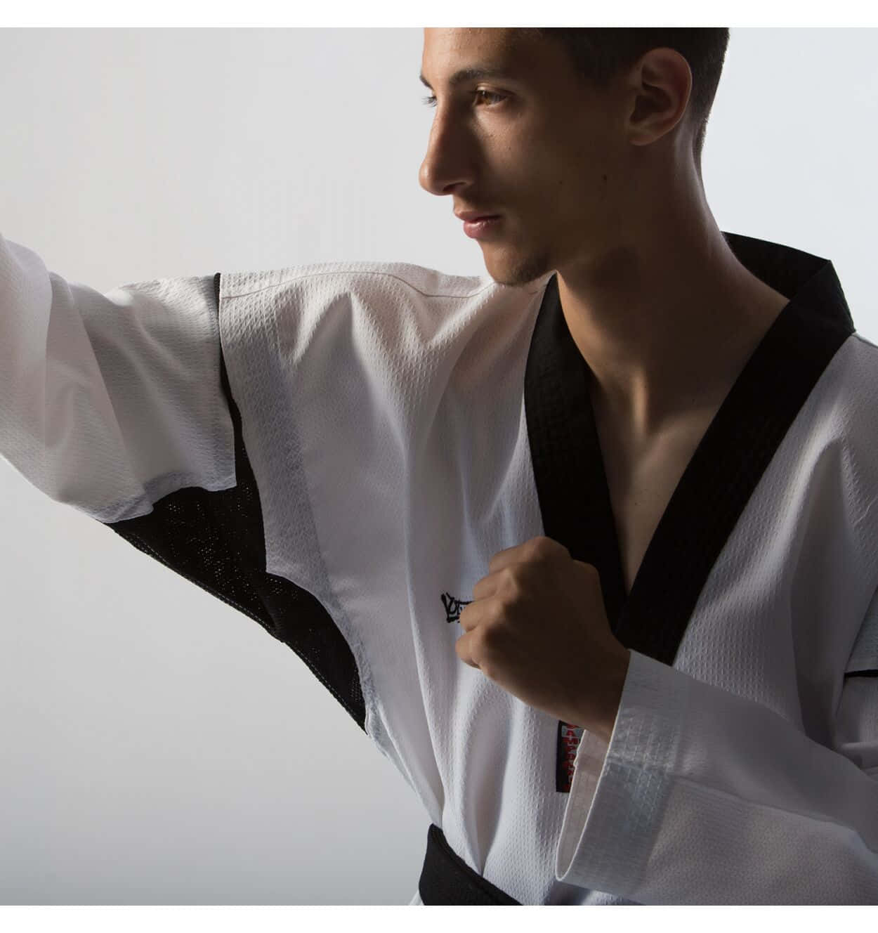 Taekwondo Uniform 桌布 壁紙 — 一位專注的武術家穿著白色道服，繫著黑帶，帶有黑色飾邊，在柔和燈光的攝影棚中出擊。