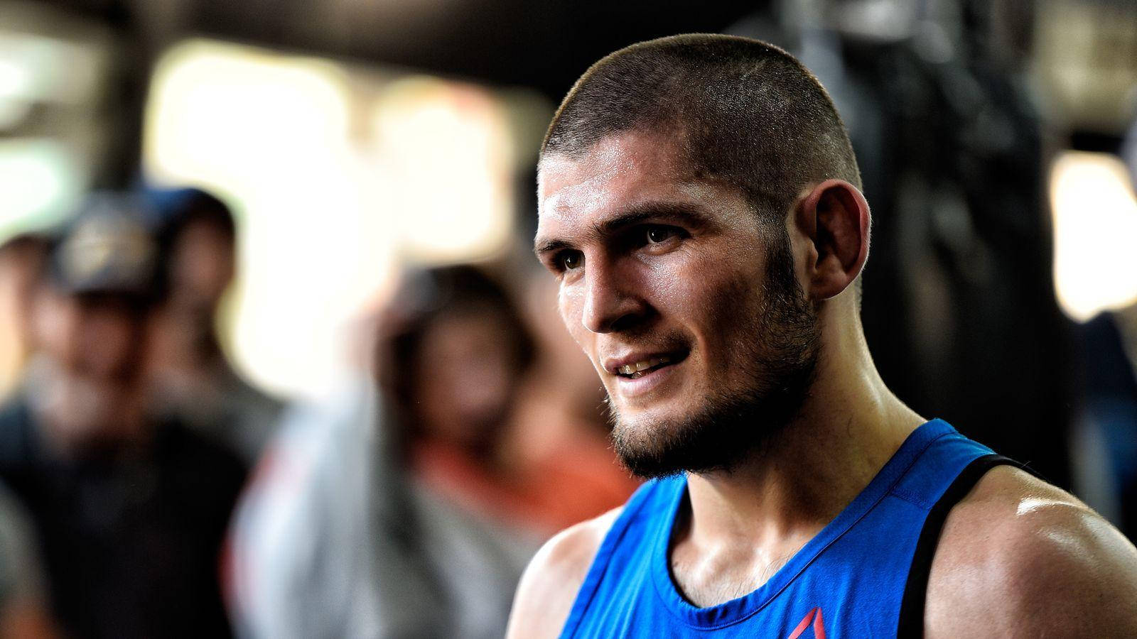 UFC 桌布 壁紙 — 一位專注的男性運動員穿著藍色背心，在訓練期間微笑，背景有模糊的觀眾。