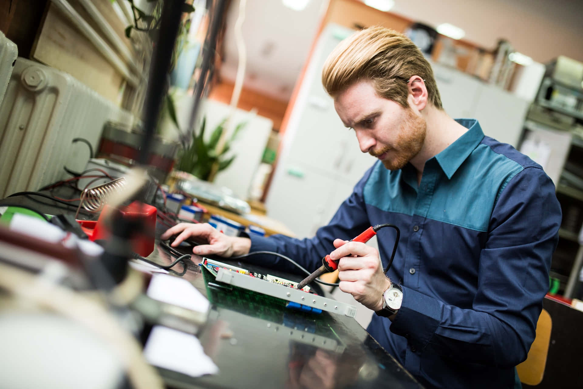 Engineer 桌布 壁紙 — 一位專注的紅髮技術員在雜亂的電子工作坊中仔細焊接電路板。