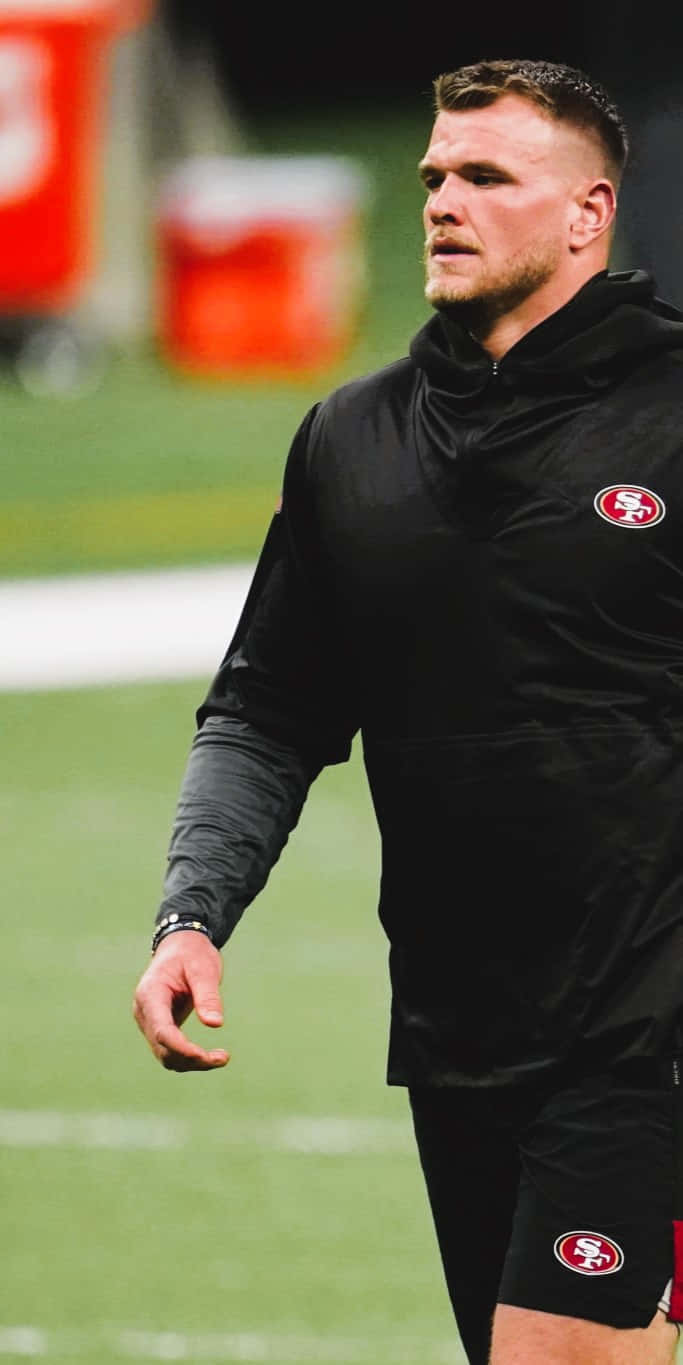 Mike Mcglinchey 桌布 壁紙 — 一位專注的美式足球員身穿黑色三藩市四九人裝備，站在綠色球場上，球場燈光照射。