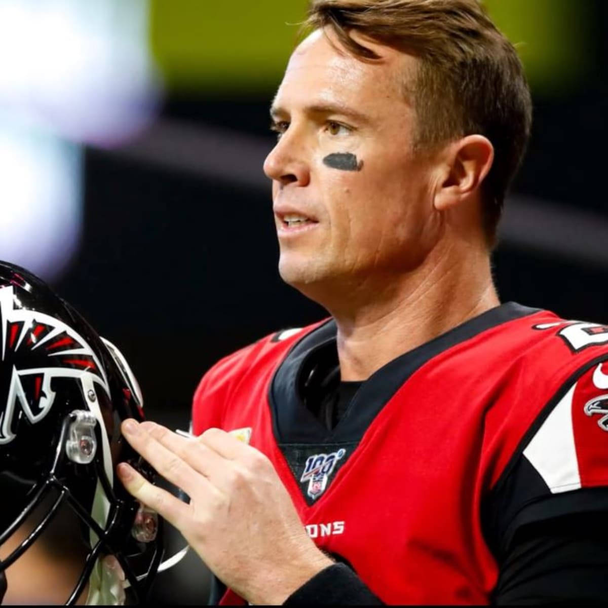 Matt Ryan 桌布 壁紙 — 一位專注的美式足球四分衛，身穿紅色亞特蘭大獵鷹隊球衣，在球場燈光下比賽時拿著頭盔。