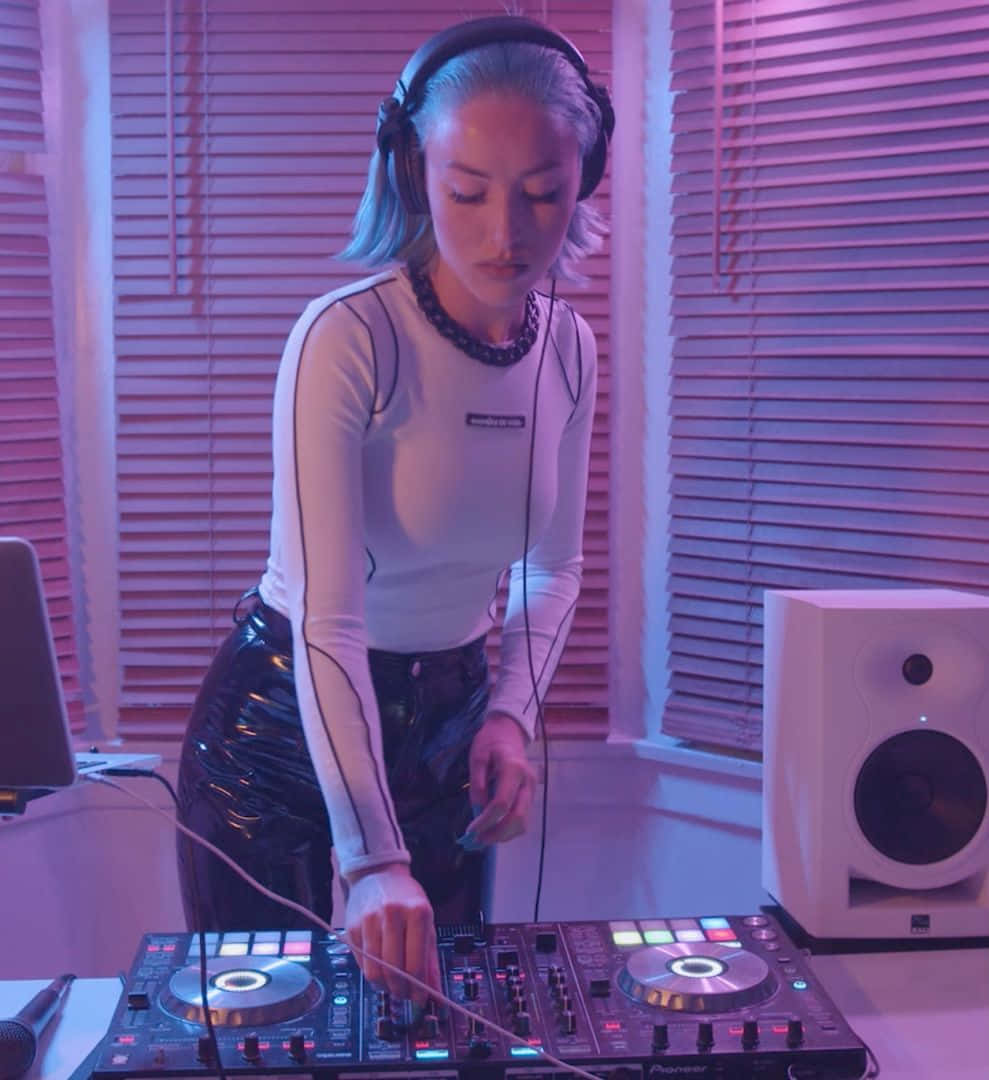 DJ 桌布 壁紙 — 一位專注的藍髮女DJ在充滿活力的粉紅和紫色燈光下，用Pioneer DJ控制器混音。