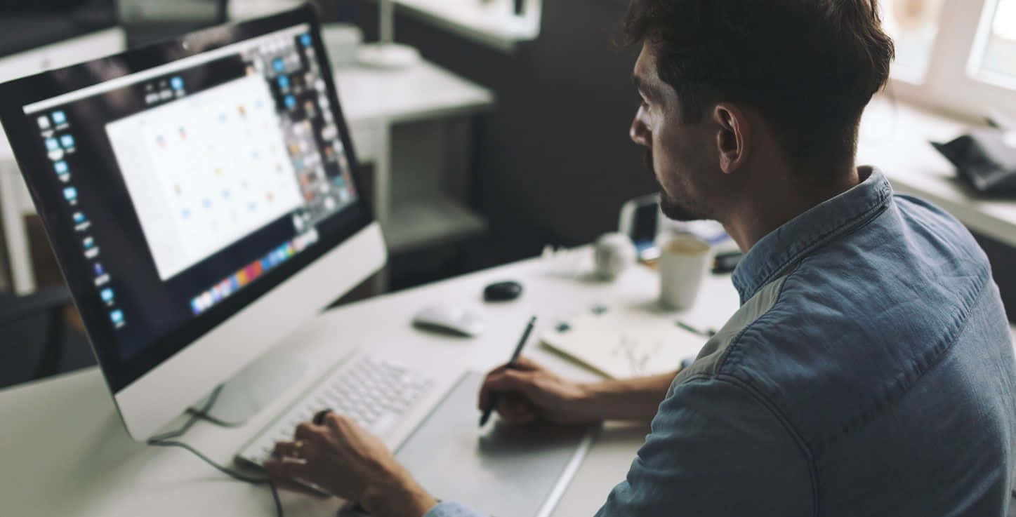 Website 桌布 壁紙 — 一位專注的設計師在現代工作室中使用繪圖板和電腦在時尚的辦公桌上工作。