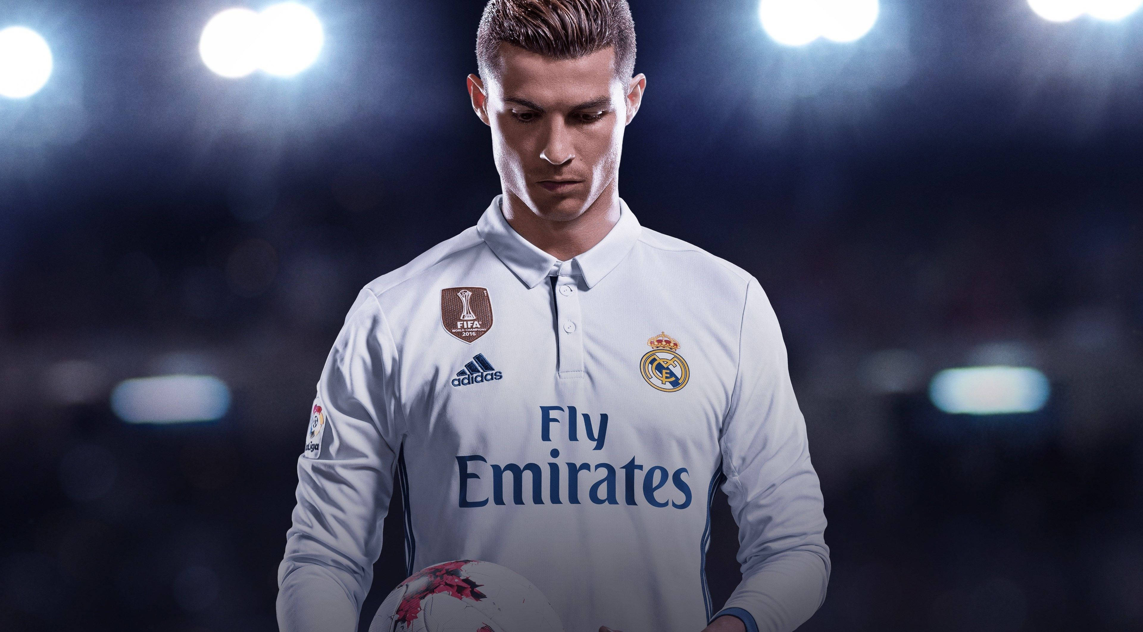 Cristiano Ronaldo 桌布 壁紙 — 一位專注的足球運動員身穿白色皇家馬德里球衣，在明亮的球場燈光下抱著足球。