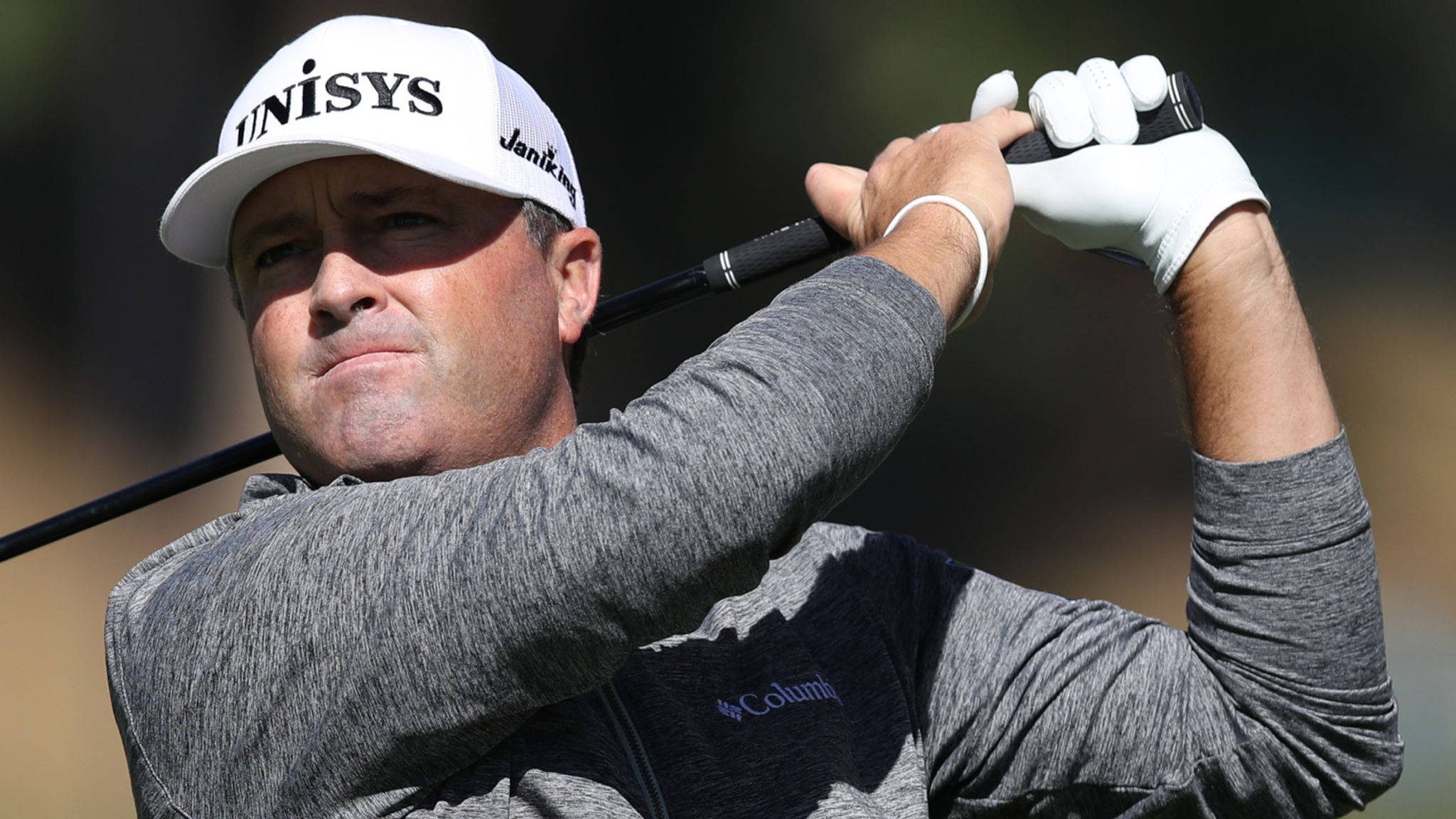 Ryan Palmer 桌布 壁紙 — 一位專注的高爾夫球手正在揮桿，戴著白色帽子，穿著灰色襯衫，背景是模糊的戶外景色。