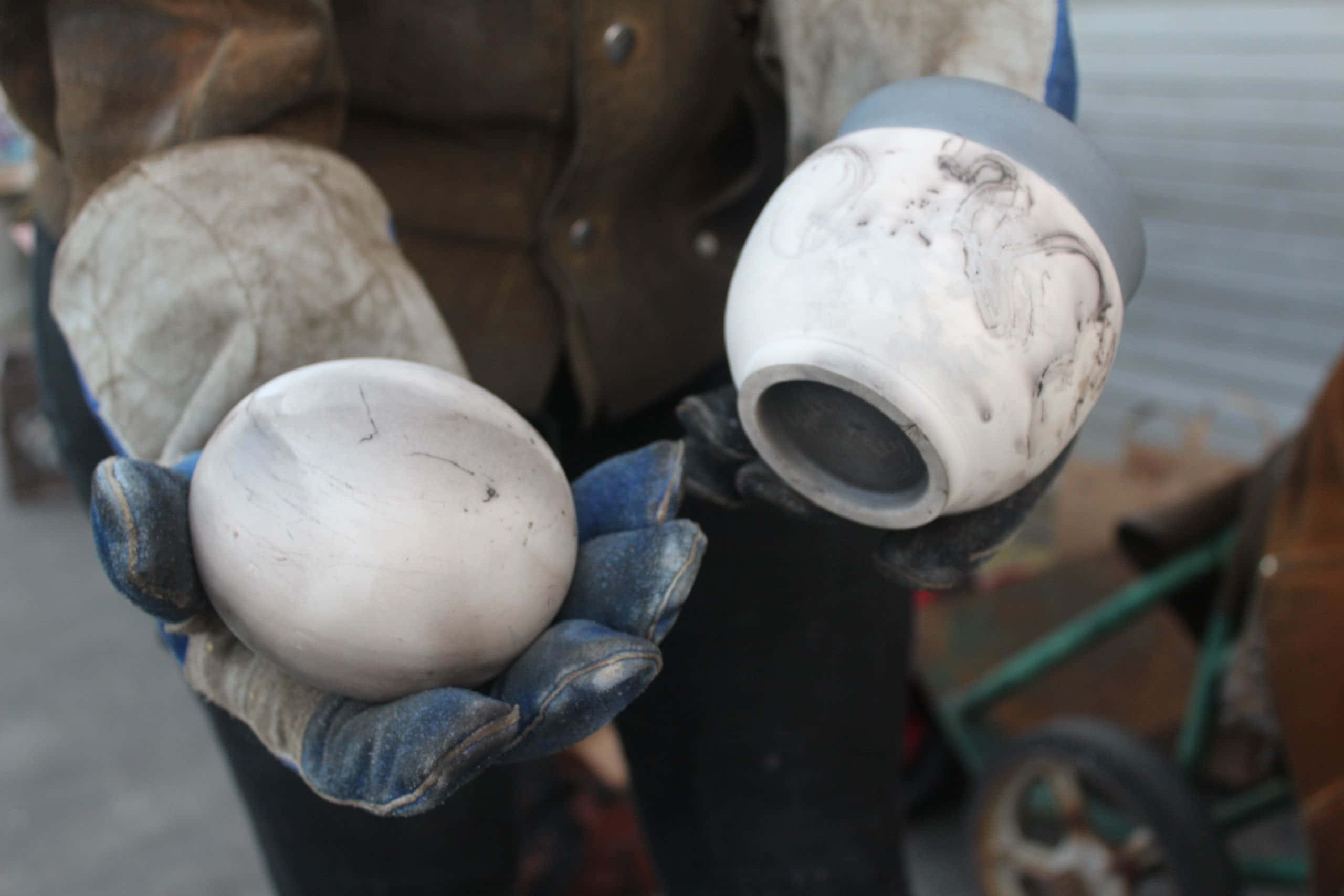 Ceramic 桌布 壁紙 — 一位工匠戴著磨損的手套，拿著兩件未完成的陶瓷作品，一件球形，一件碗形，兩件都塗有白色泥漿和深色漩渦紋。