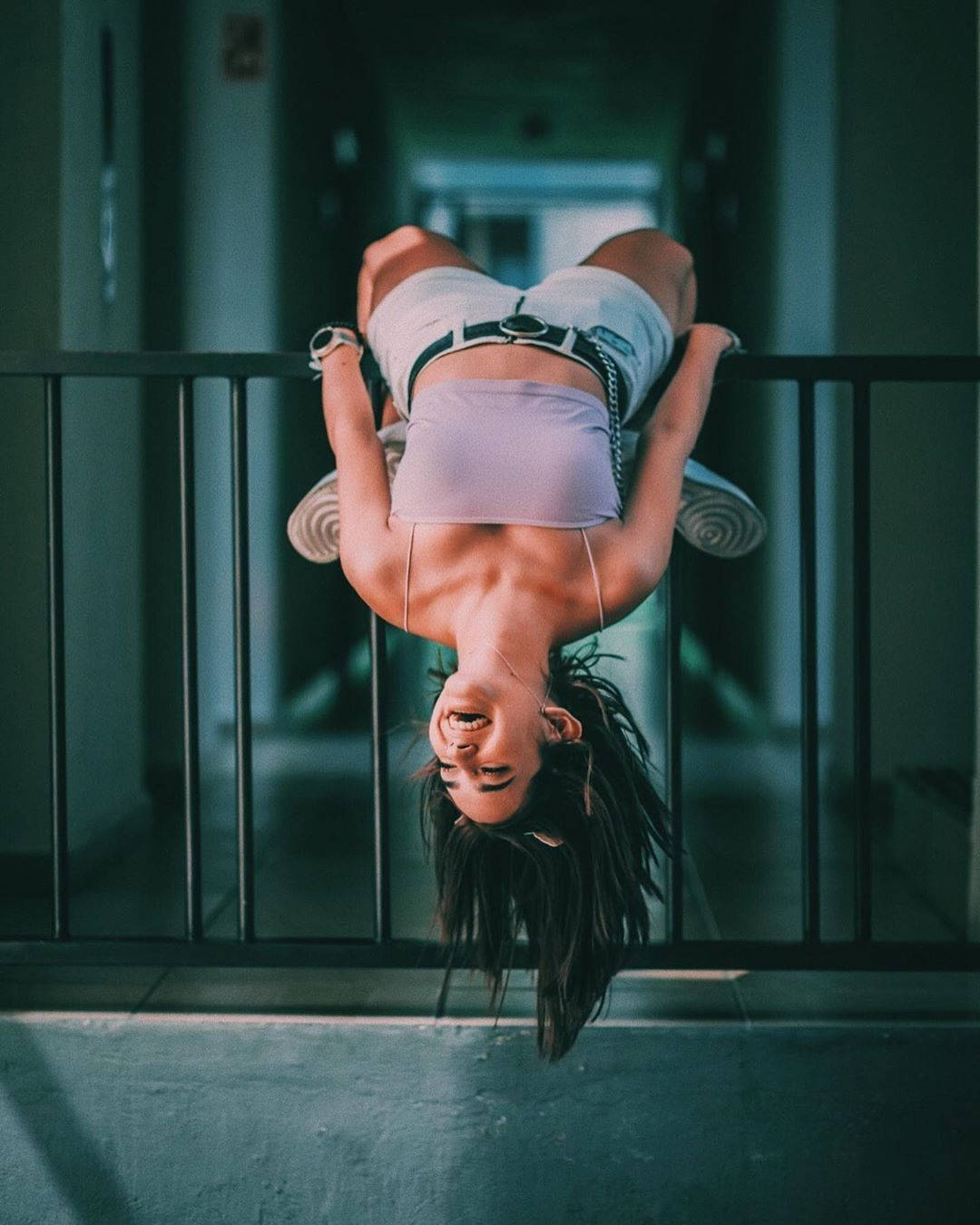 一位女子倒掛在城市走廊的欄杆上微笑。 — TikTok GIF 壁紙