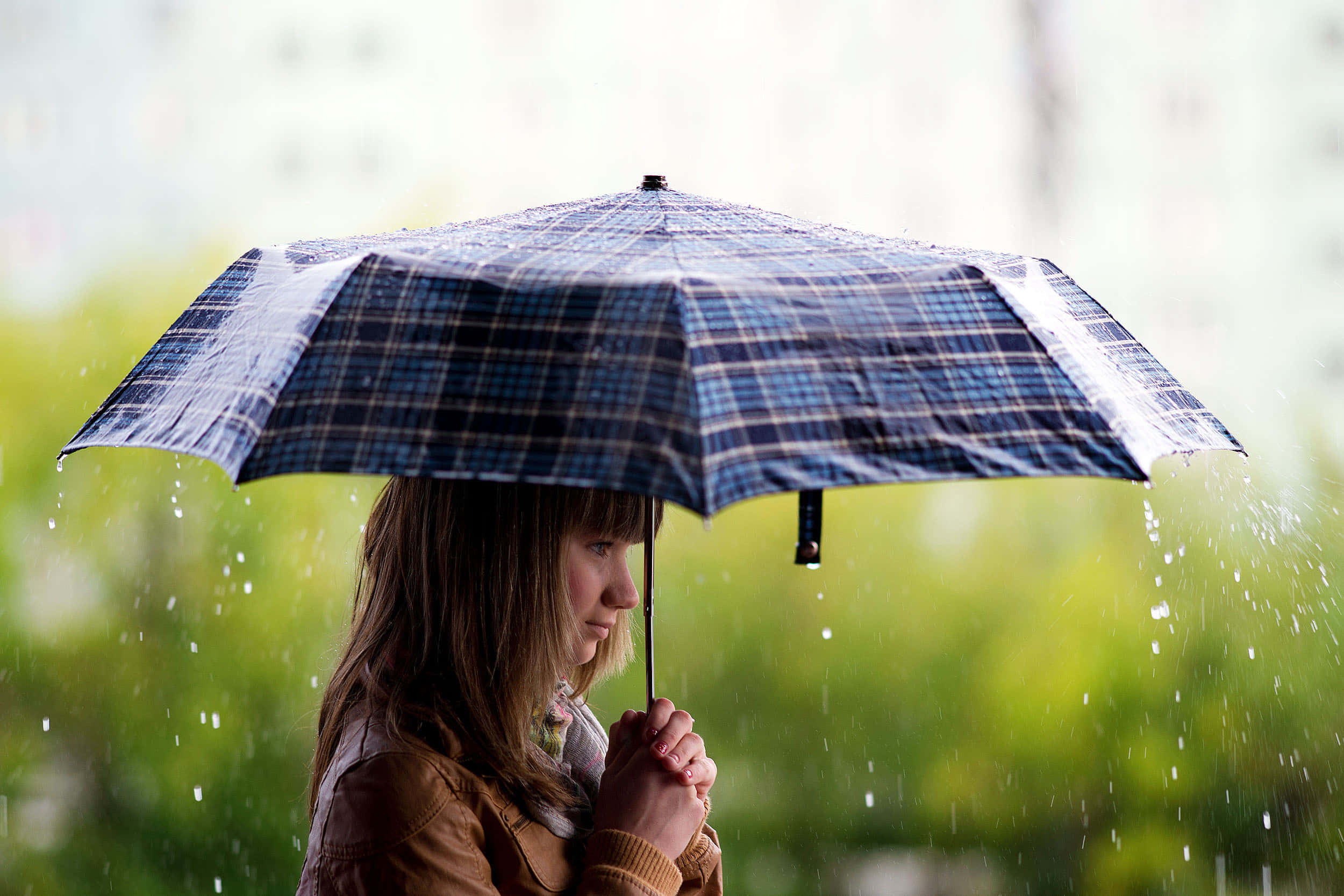 Woman 桌布 壁紙 — 一位年輕女子撐著格子雨傘，在模糊的綠色戶外環境中遮擋雨水。
